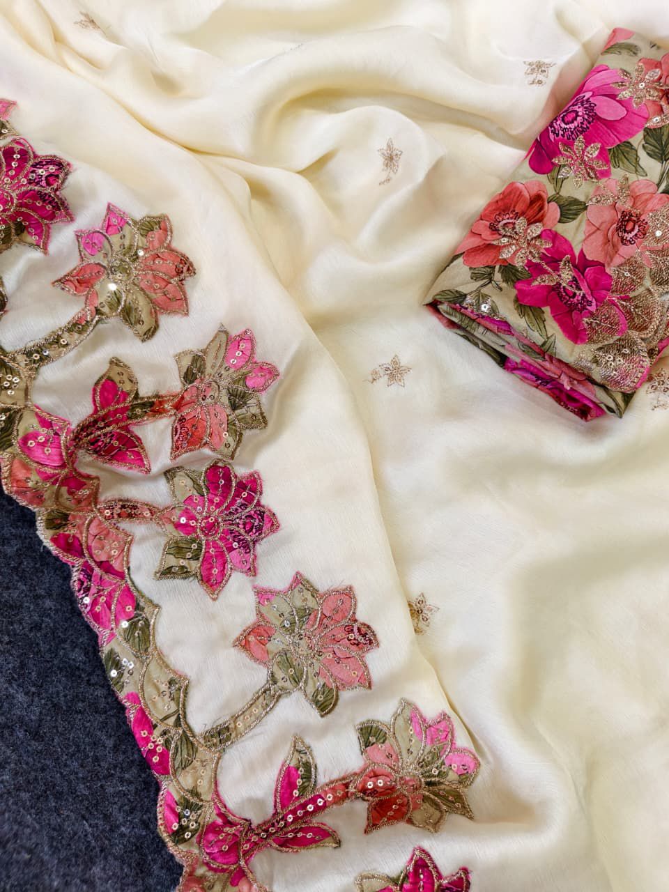 White fabric with pink floral embroidery and gold accents on a dark surface