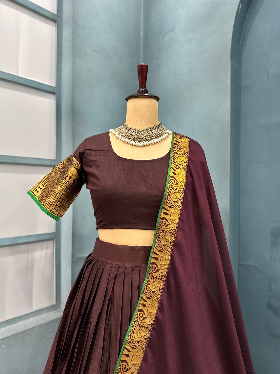 Brown traditional outfit with gold embroidery on a mannequin against a light blue wall.