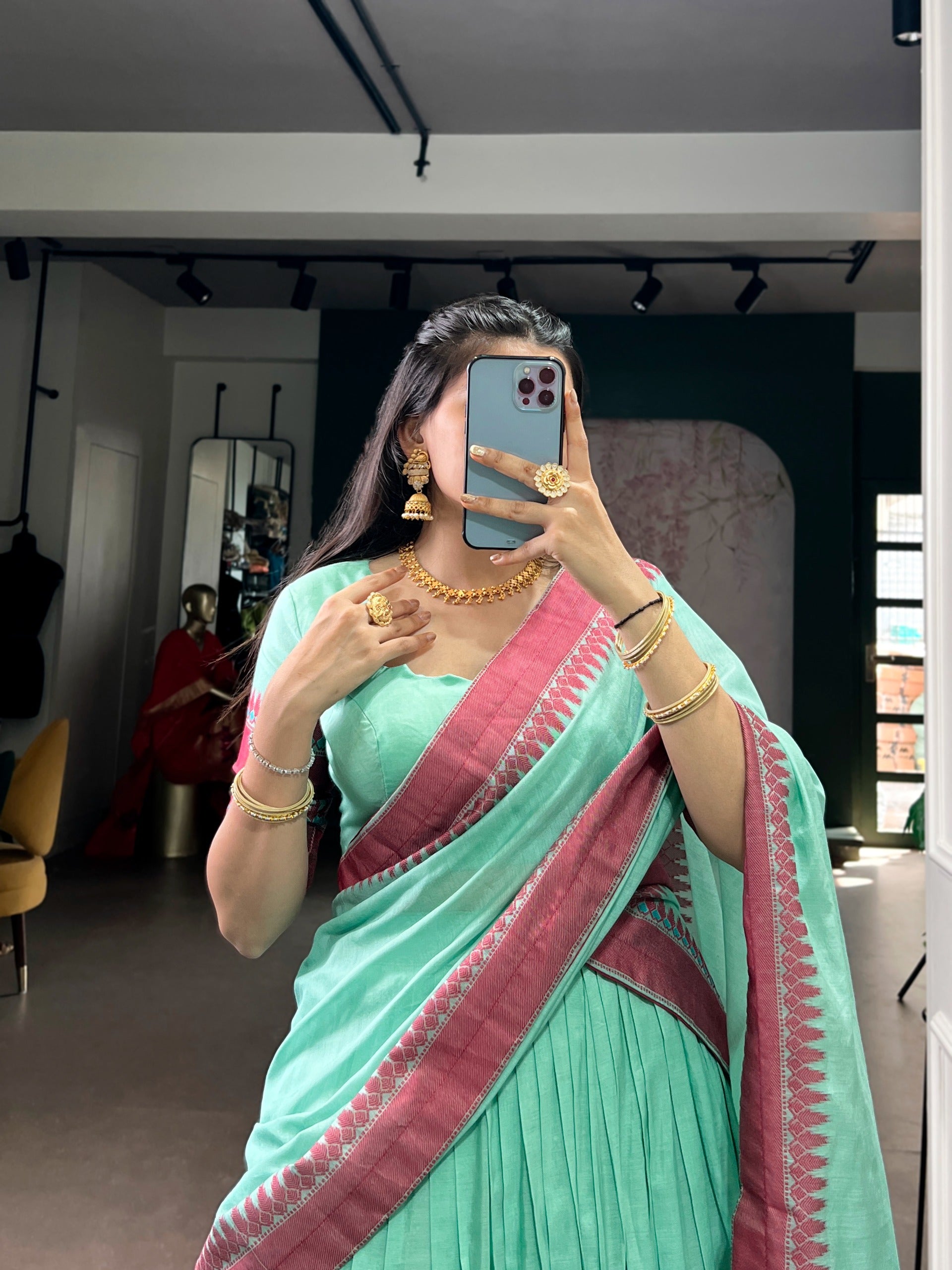 Person wearing a cyan saree with pink border, posing in front of a mirror.