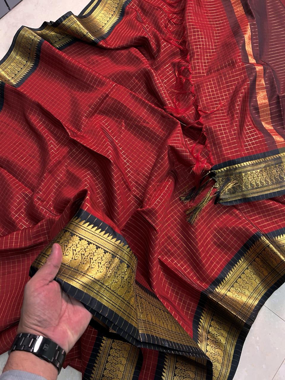 Red saree with gold and black border held by a hand on a white background