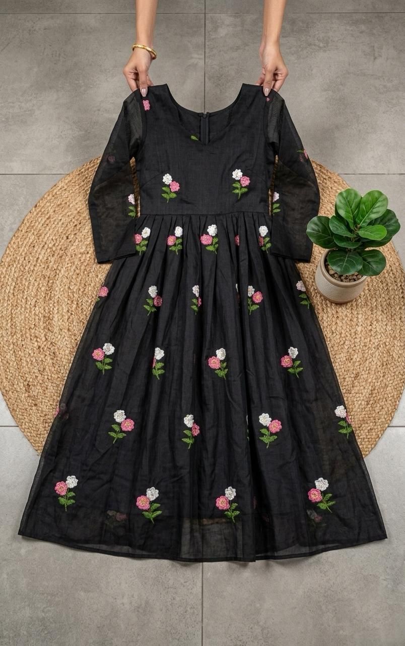 Black dress with floral embroidery held by a person on a floor.