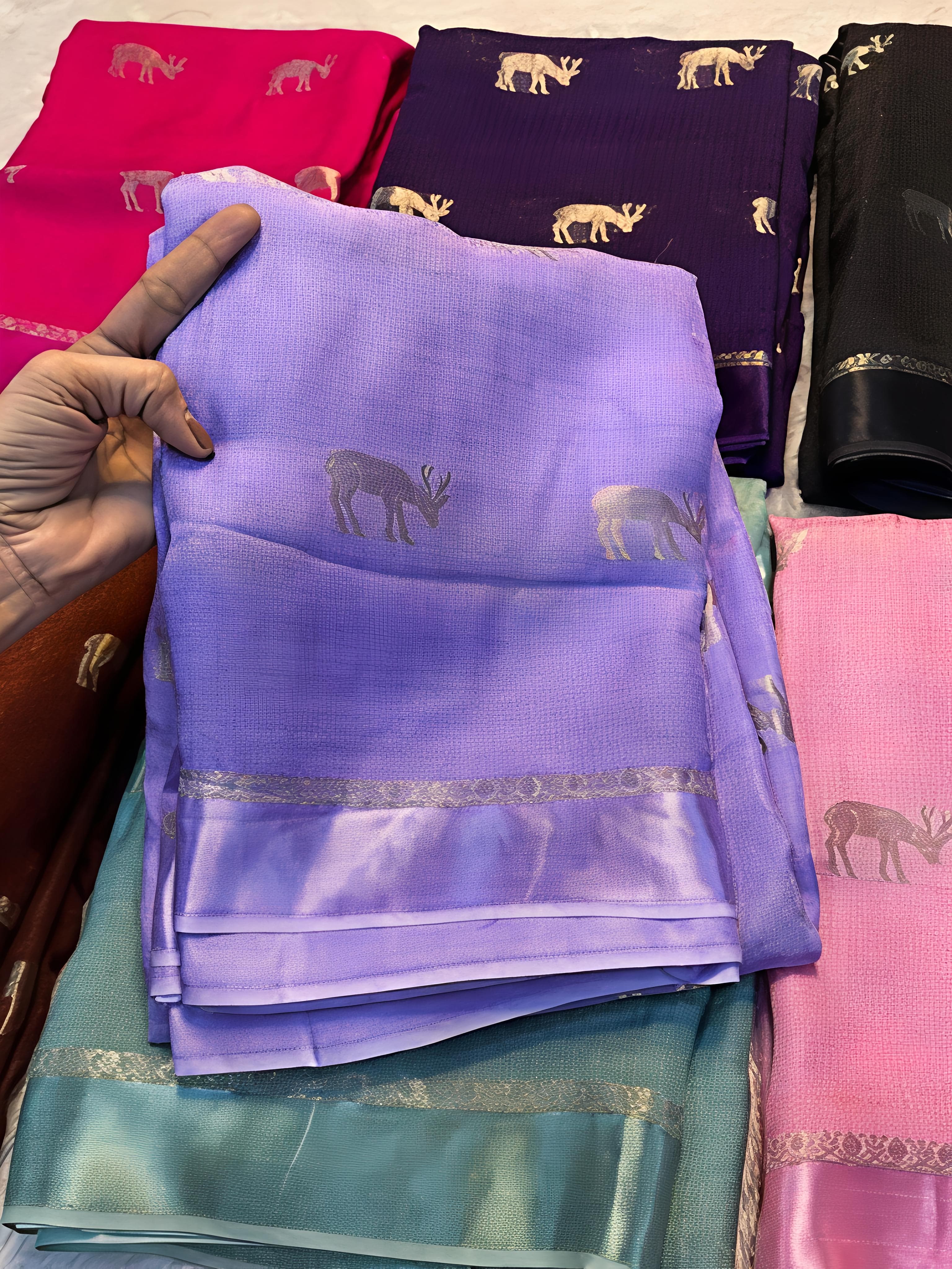 Lavender saree with deer patterns held by a hand, surrounded by other colorful sarees.