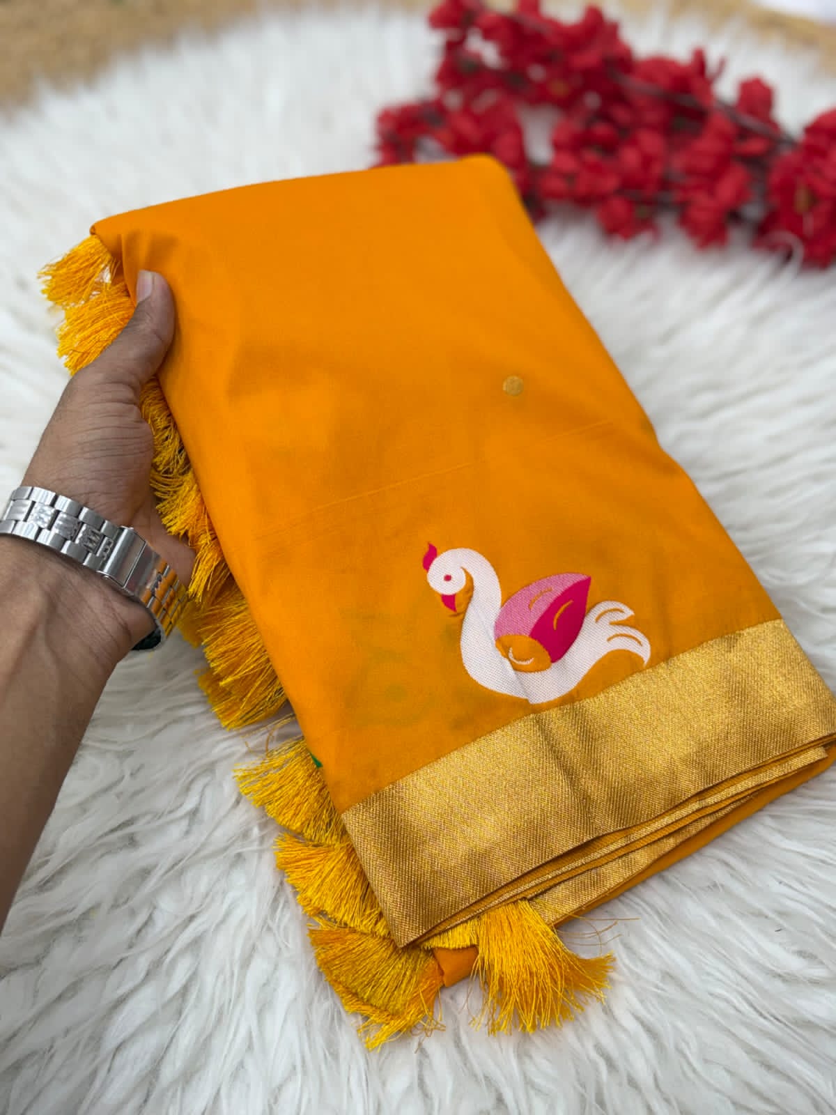 Yellow fabric with tassels and a swan design held by a hand on a surface.