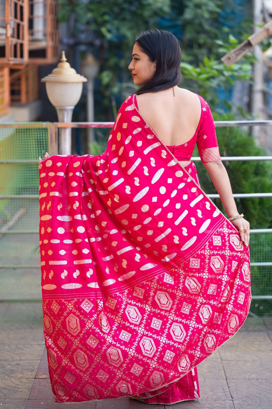 Woman wearing a pink saree with white patterns on a balcony.