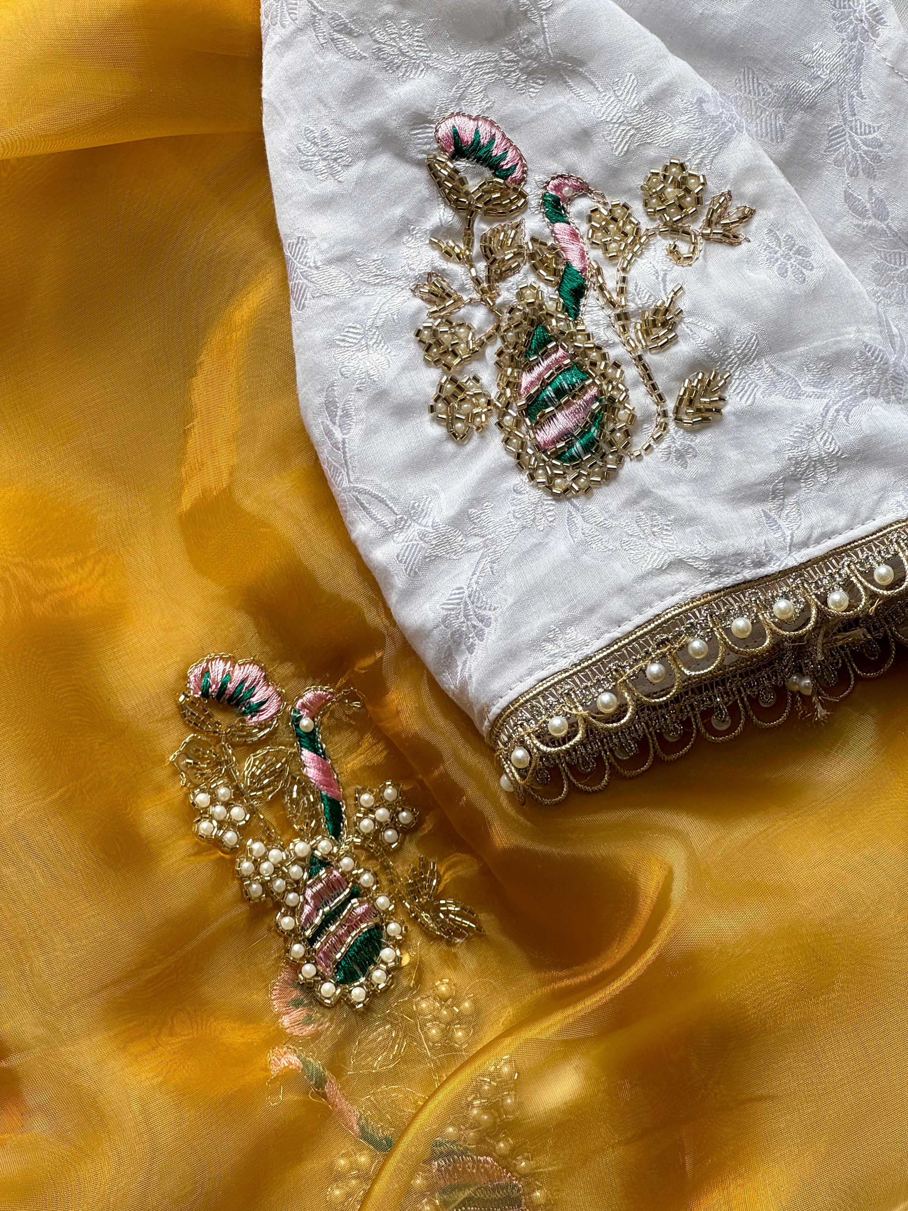 White embroidered fabric with gold and green details on a mustard yellow fabric background