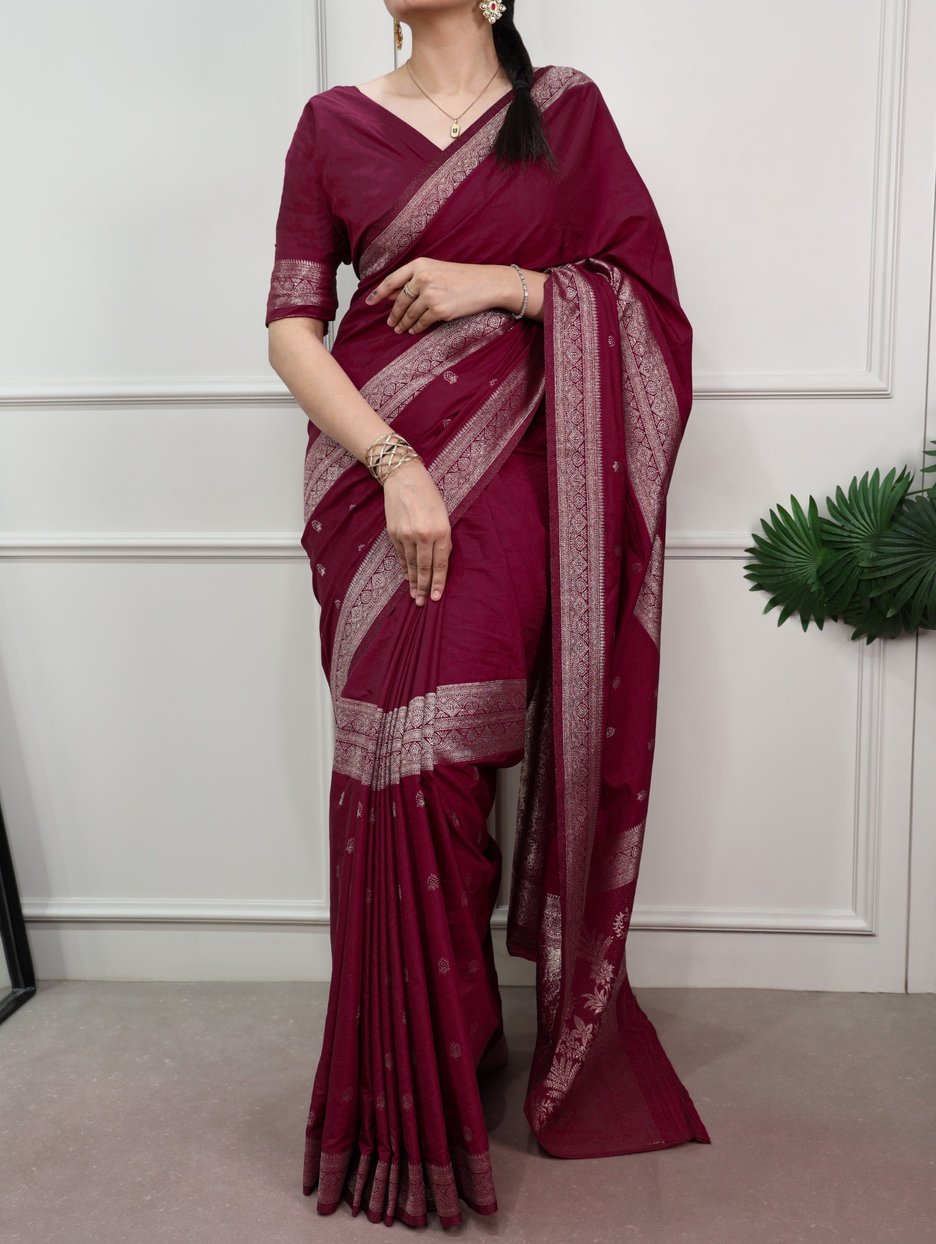 Woman wearing a maroon saree with white patterns against a white wall.