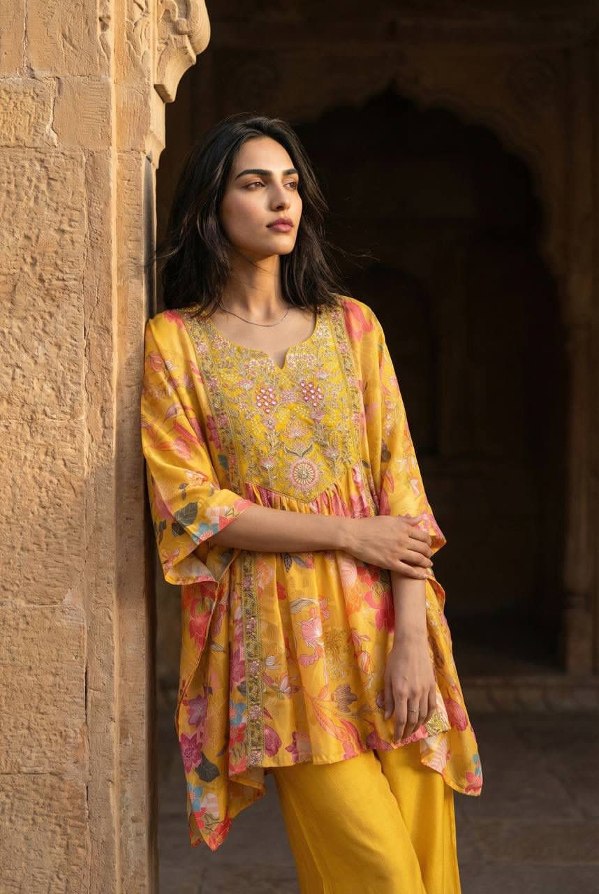 Woman in a yellow and traditional outfit standing against a stone wall.