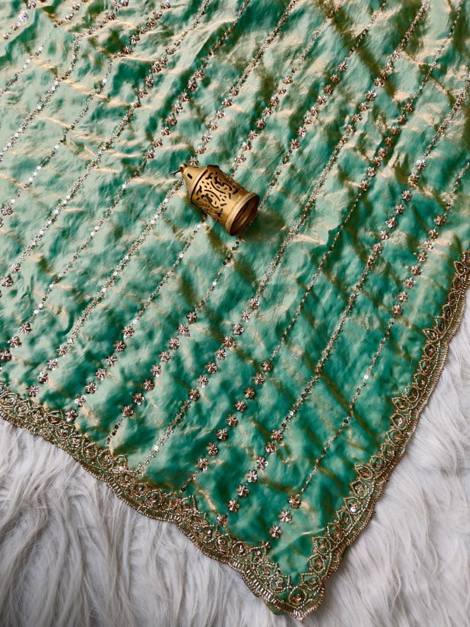 Light Green fabric with gold embroidery and a decorative gold object on a surface