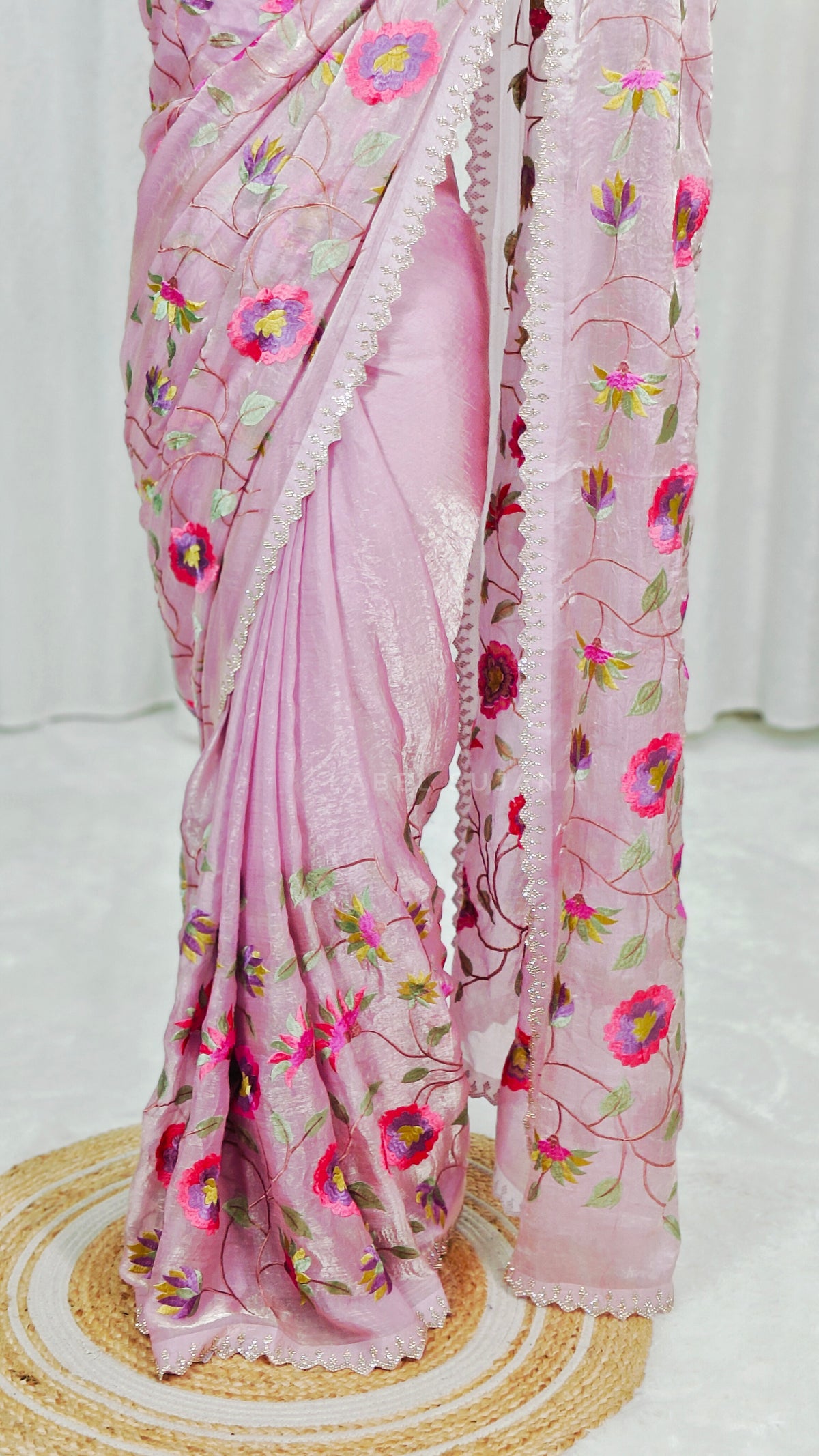 A woman wearing a baby pink saree with colorful floral embroidery and a matching embroidered blouse
