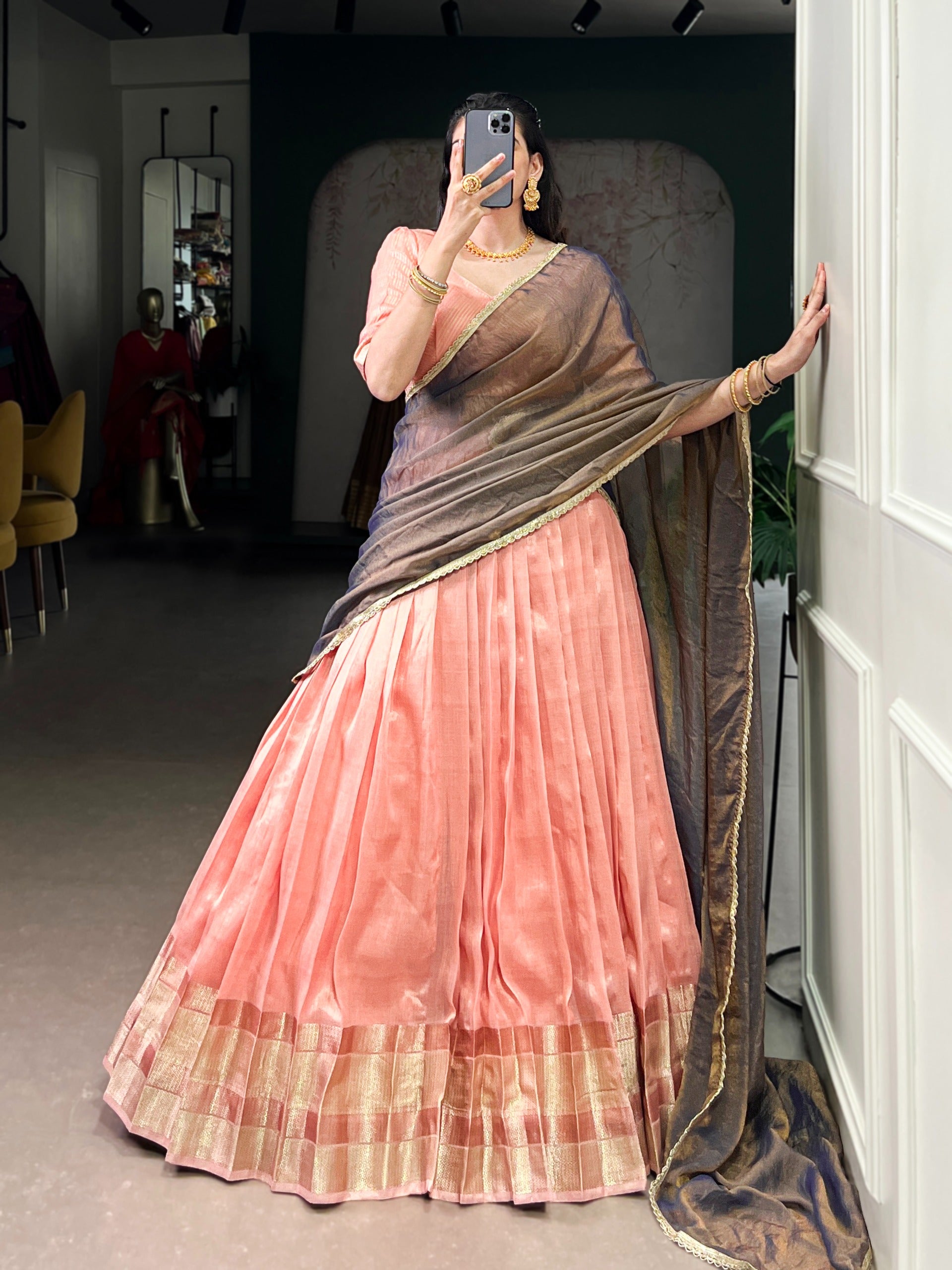 Woman in a peach saree with a dark brown border standing in a room.