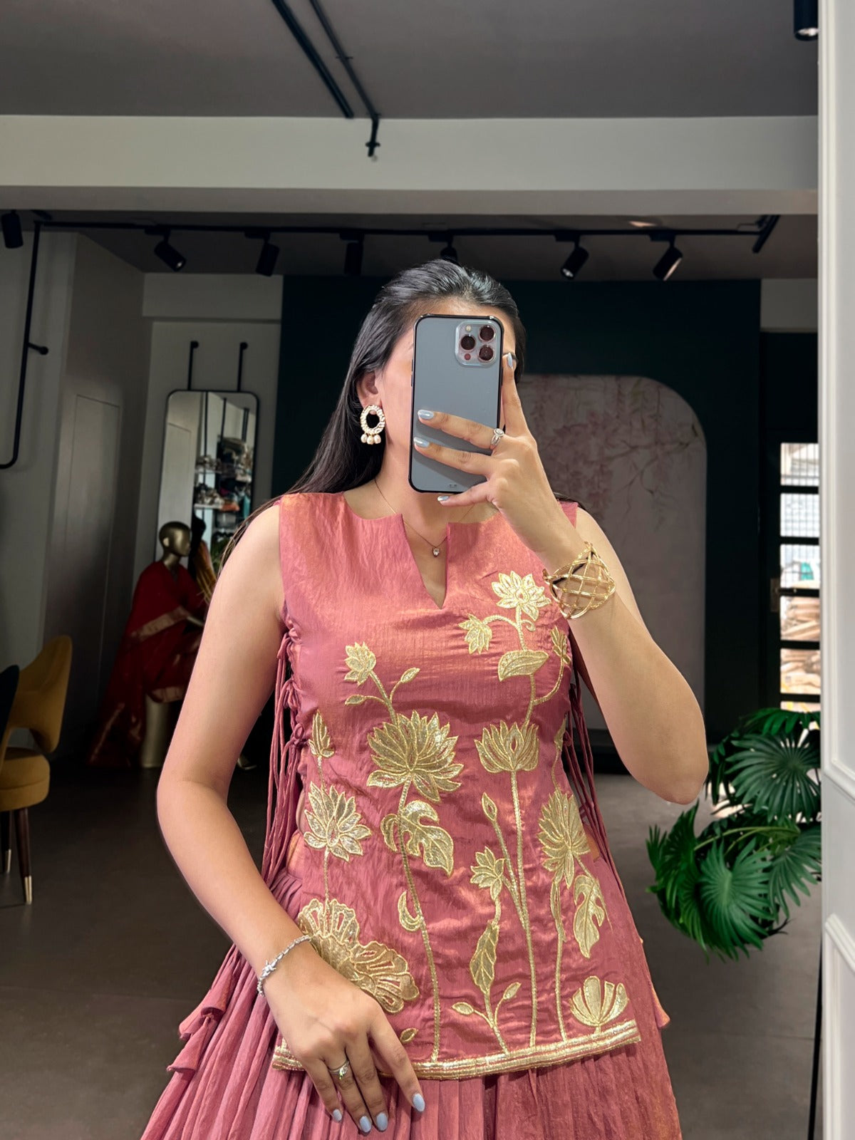 Woman taking a mirror selfie wearing a peach dress with gold floral embroidery in an indoor setting.