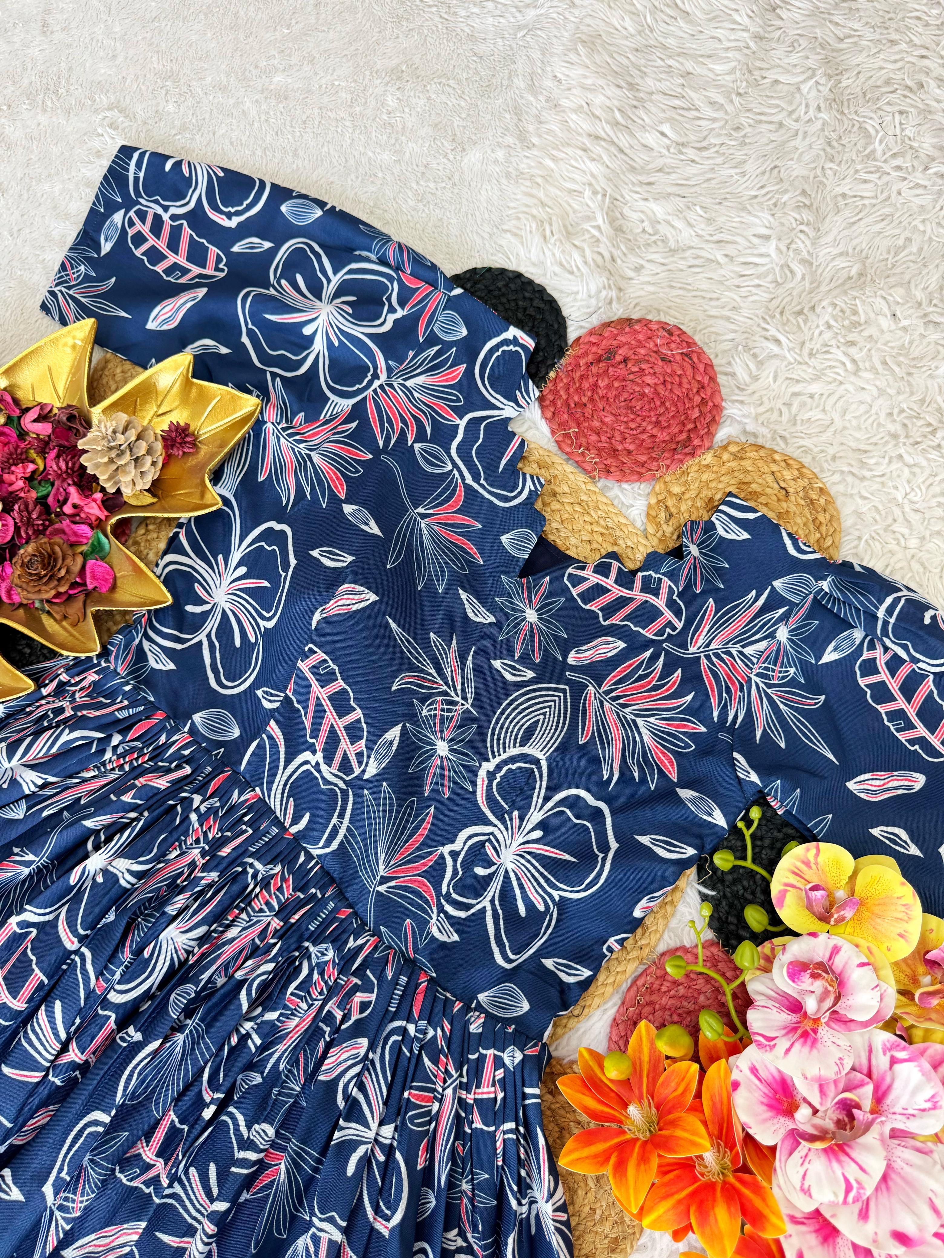 Navy dress with white floral pattern on a textured surface with flowers and pom-poms.