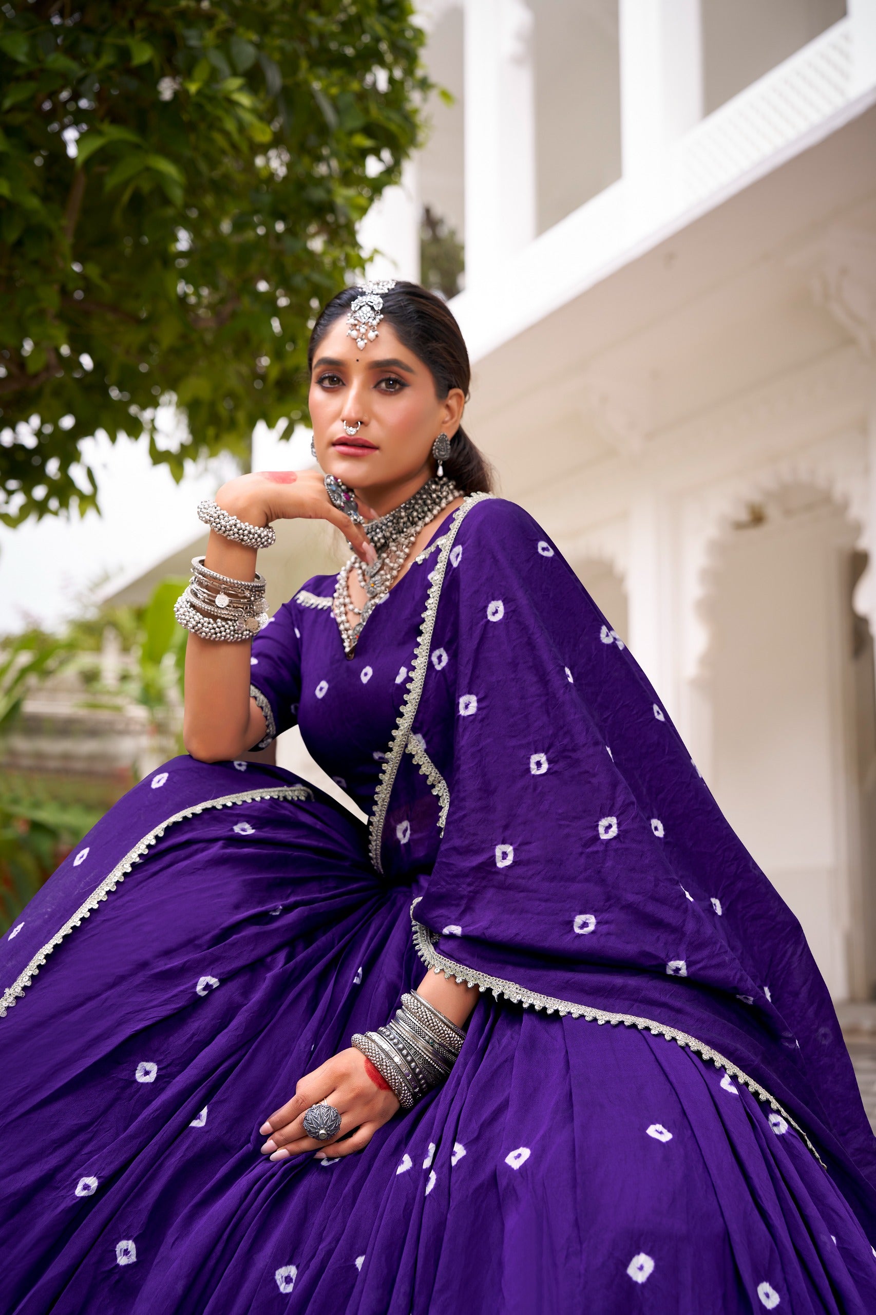 Woman in a purple traditional outfit with jewelry, standing outdoors.