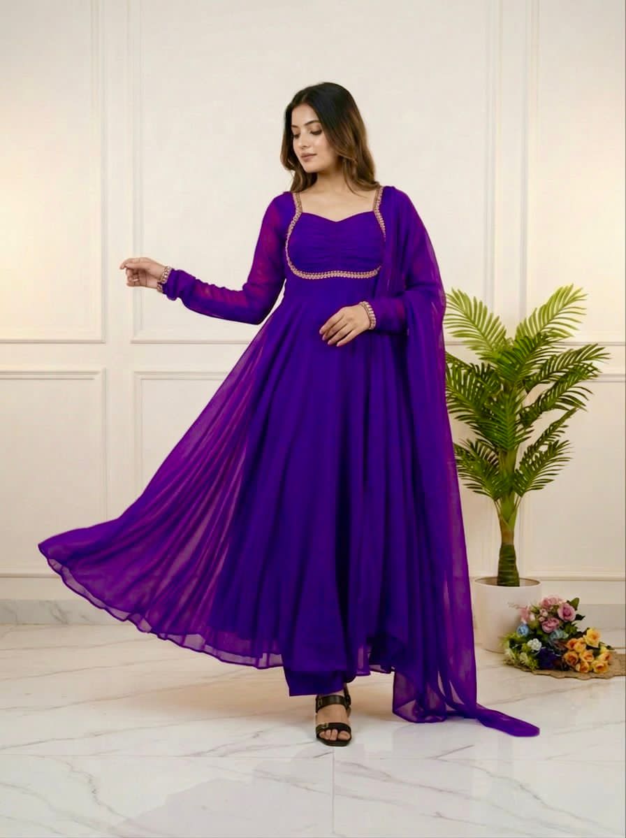 Woman wearing a purple dress standing in a room with a plant and flowers.