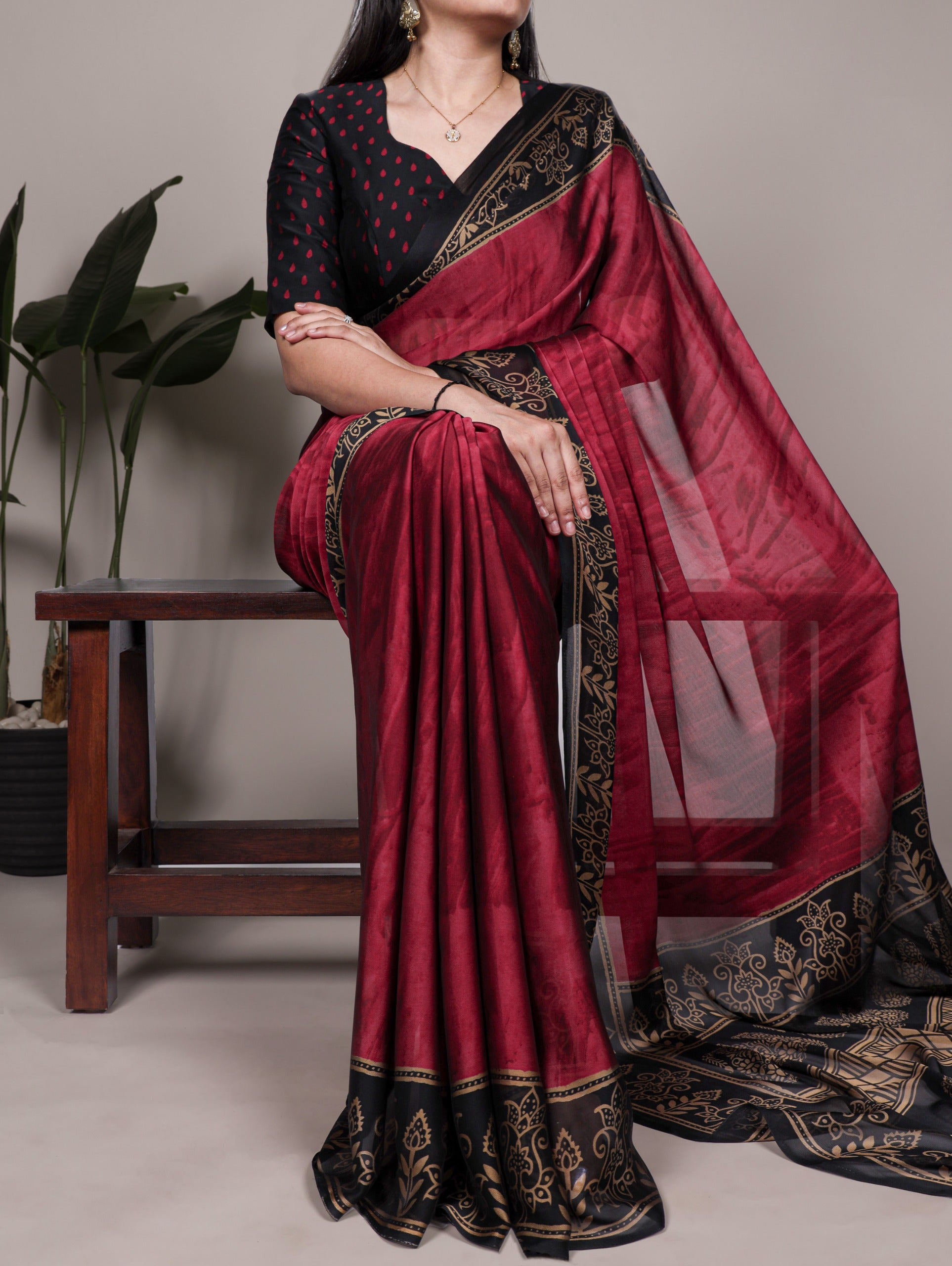 Woman wearing a maroon saree with black border, sitting on a chair.
