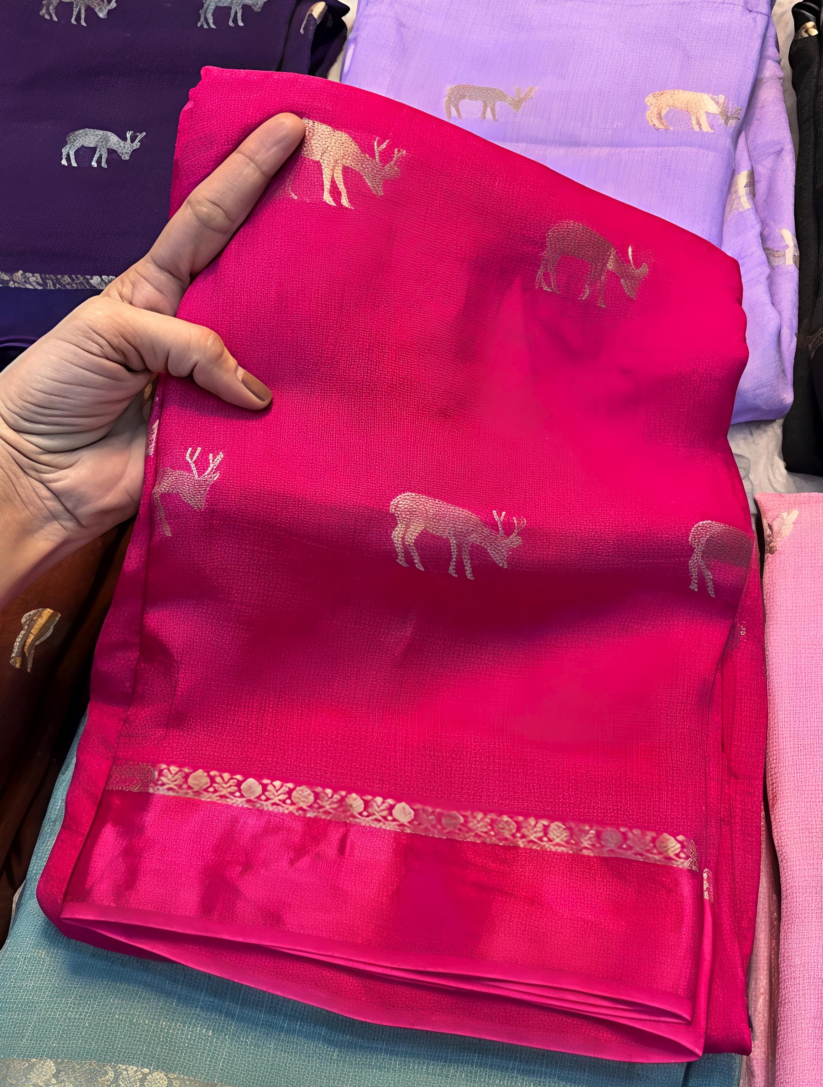Rani Pink fabric with deer patterns held by a hand, with other fabrics in the background.