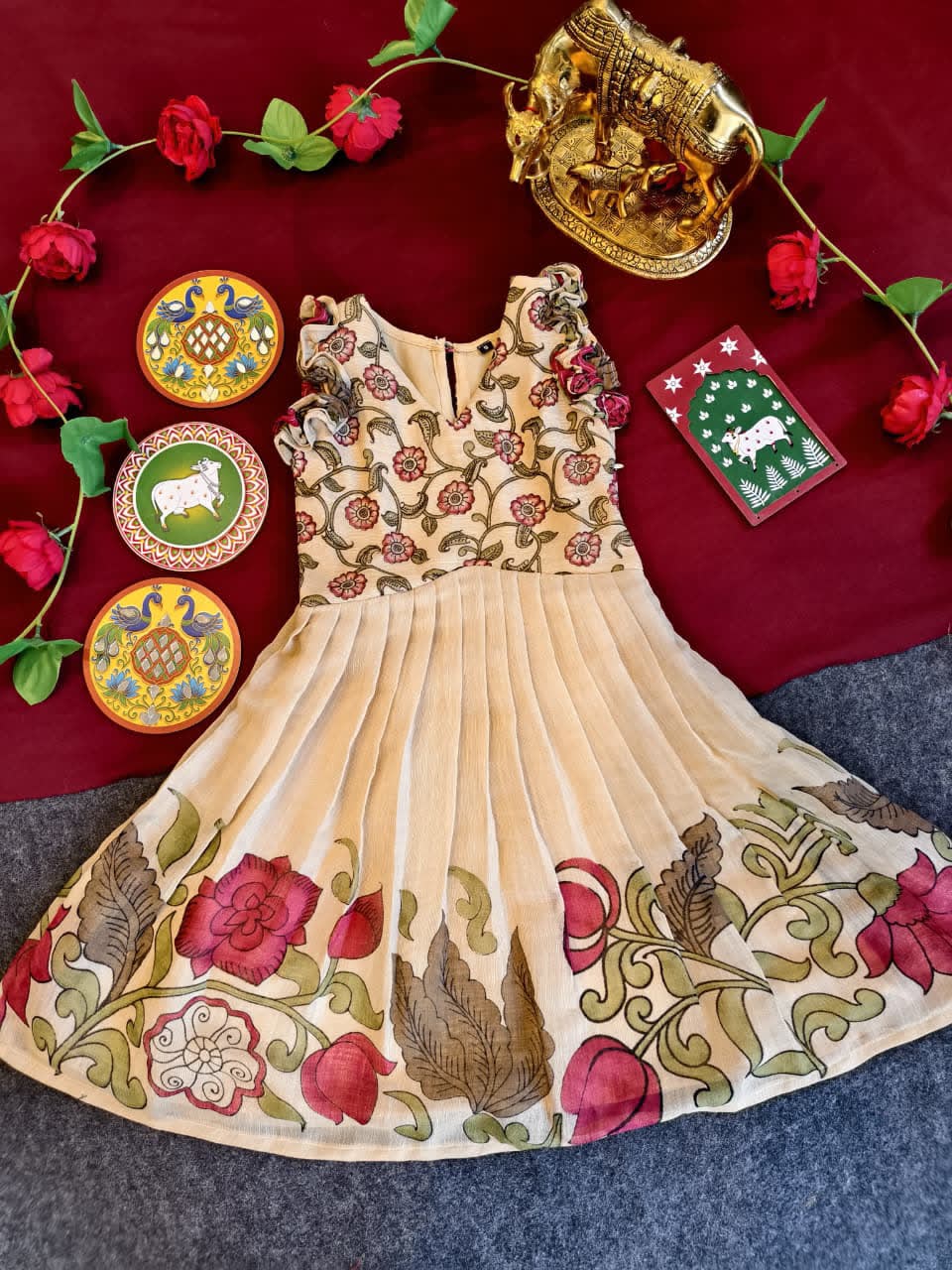 Beige embroidered dress with floral patterns on a red fabric background with decorative items.