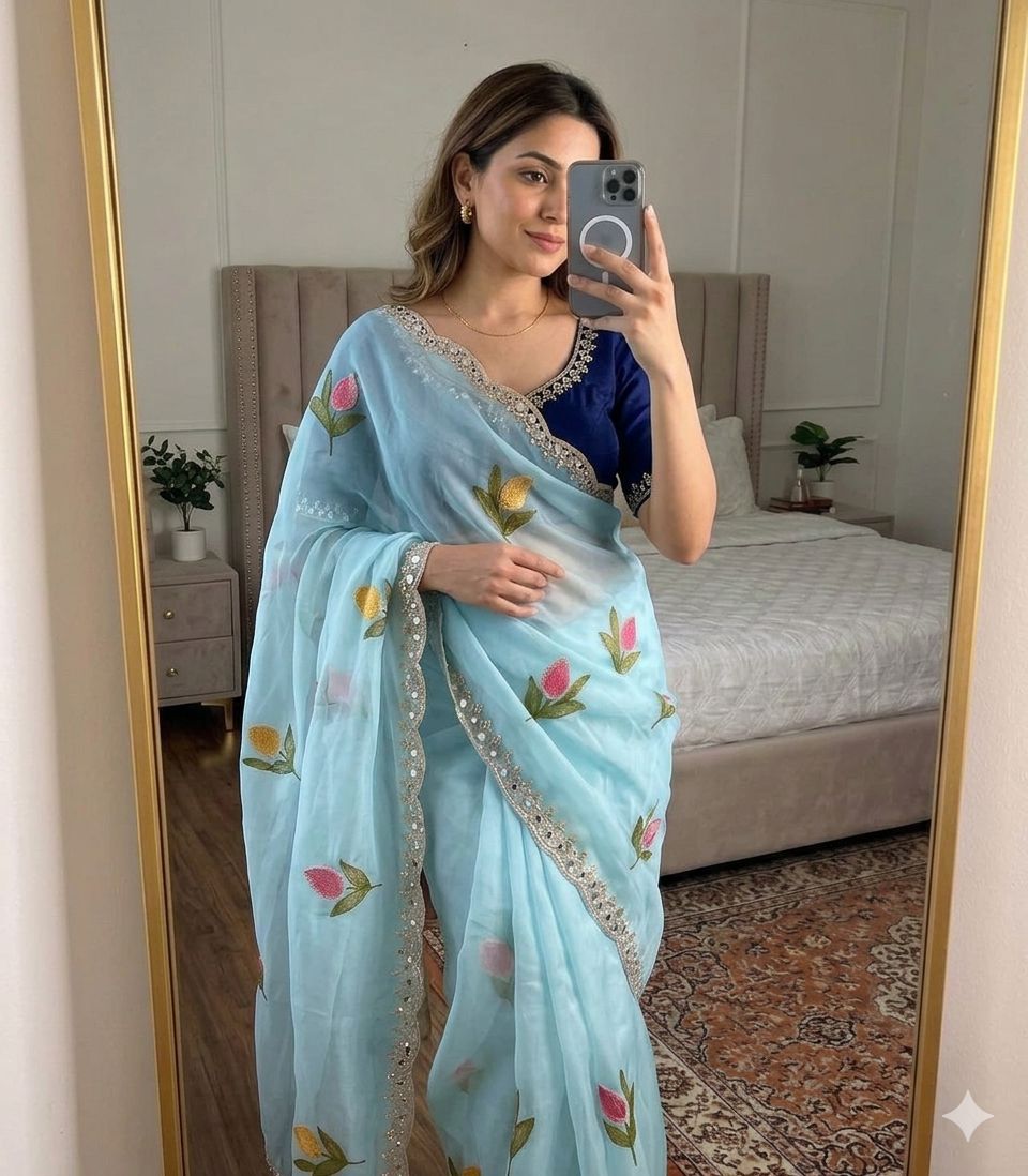 Woman wearing a sky blue saree with floral patterns in a bedroom setting.