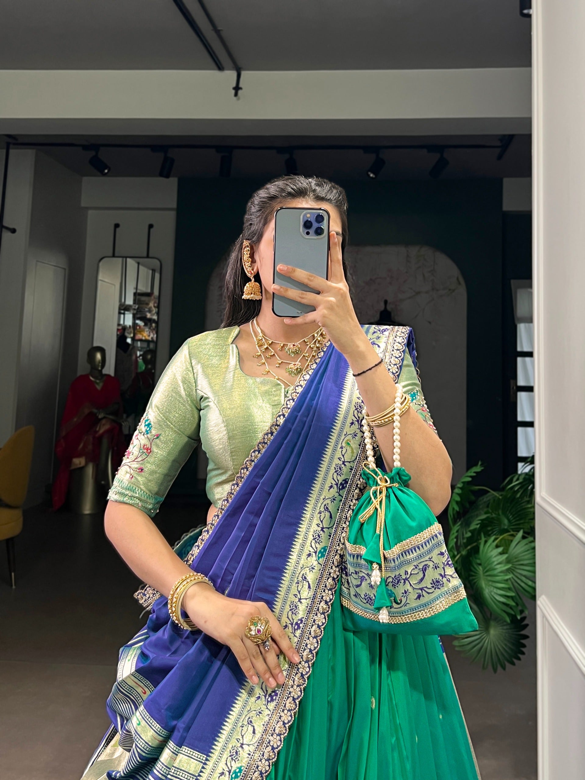Woman taking a mirror selfie wearing a cyan saree with jewelry.
