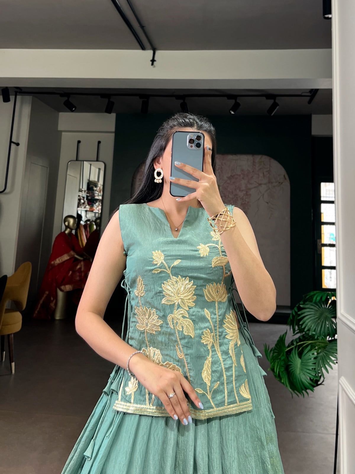 Woman taking a mirror selfie wearing a sea green embroidered dress in an indoor setting.