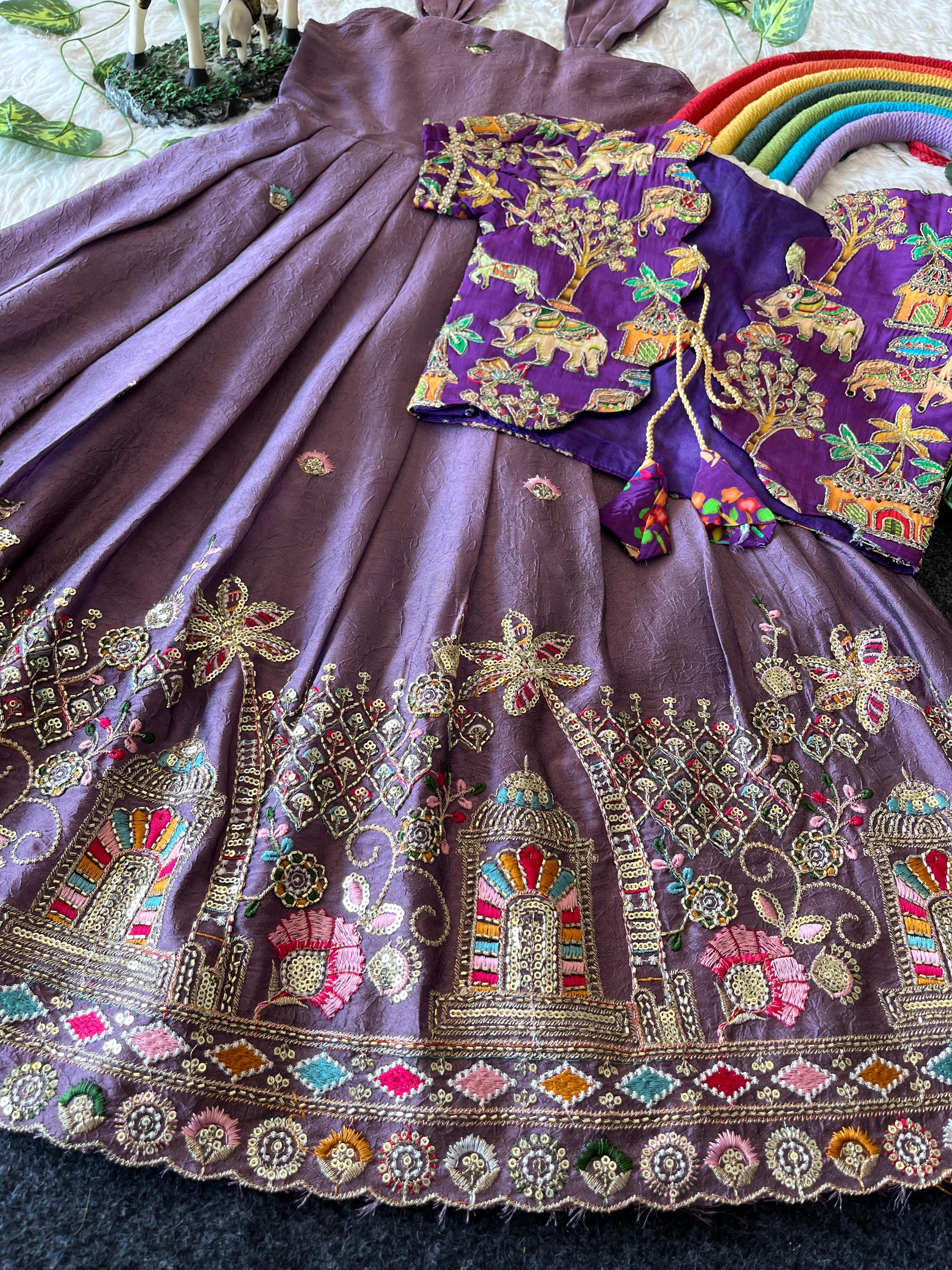 Lavender fabric with intricate gold embroidery and colorful patterns on a textured surface.