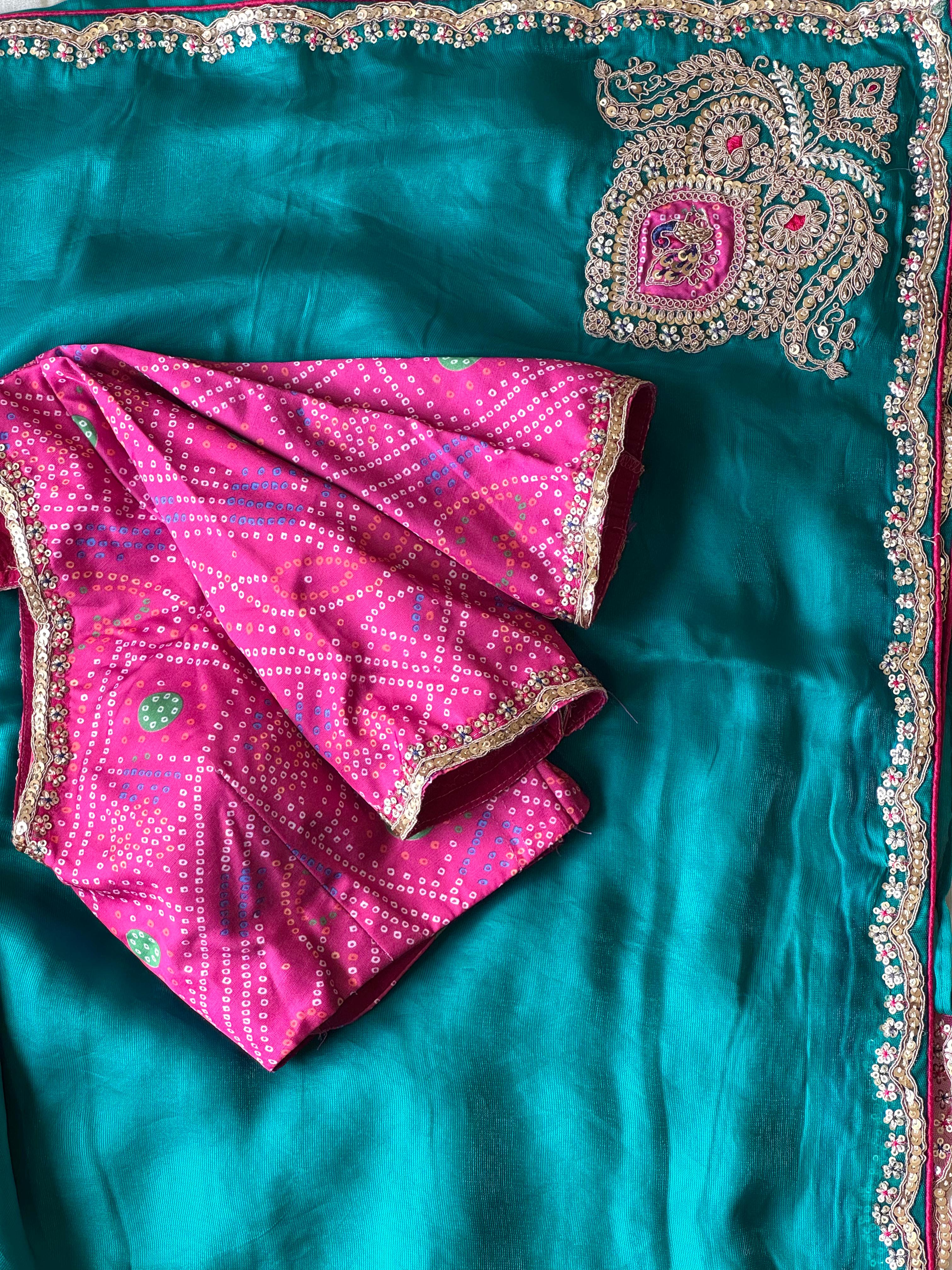 Teal blue saree with pink blouse and decorative border on a matching fabric background