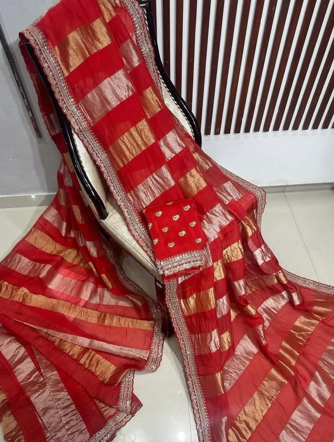 Red and gold saree draped over a chair with a white floor and wall in the background.