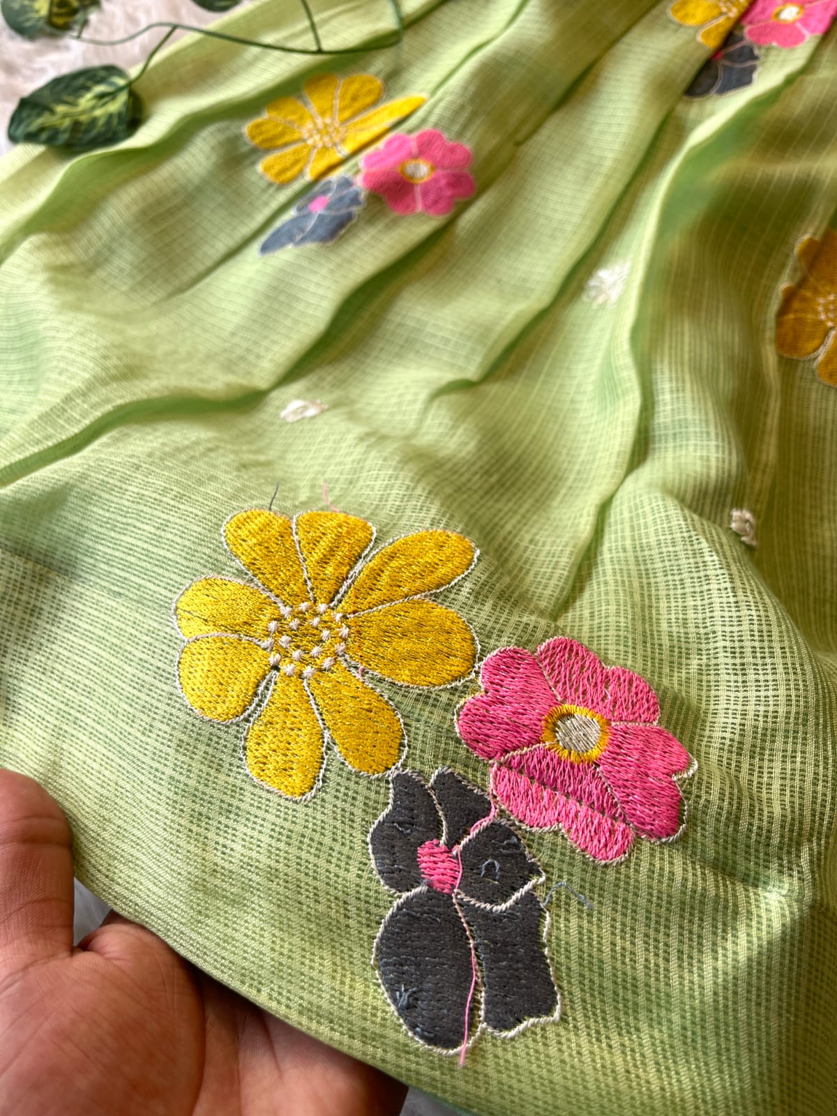 Pista fabric with embroidered flowers and a hand holding it