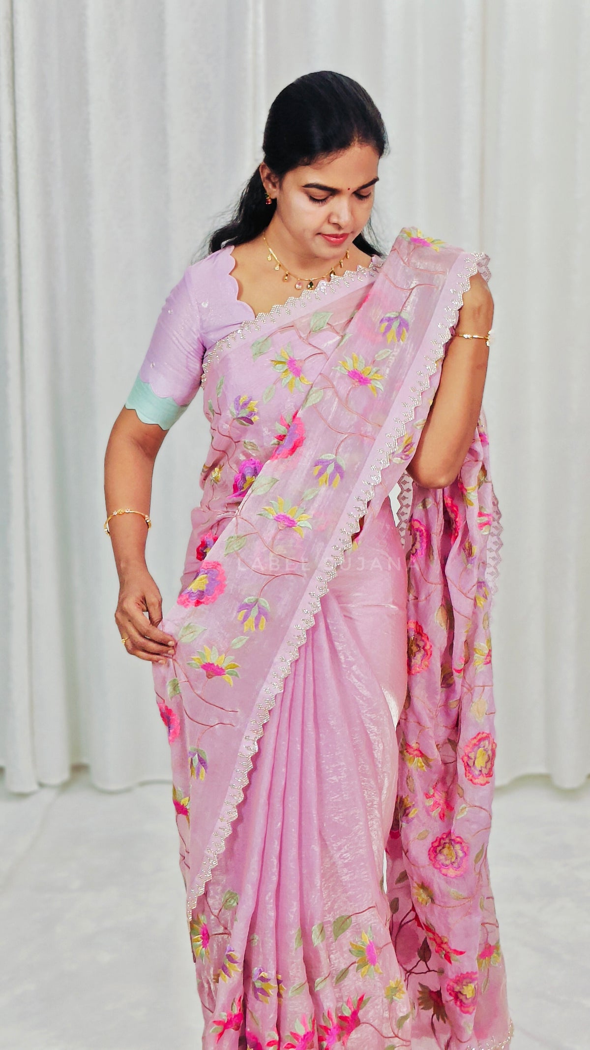 A woman wearing a baby pink saree with colorful floral embroidery and a matching embroidered blouse