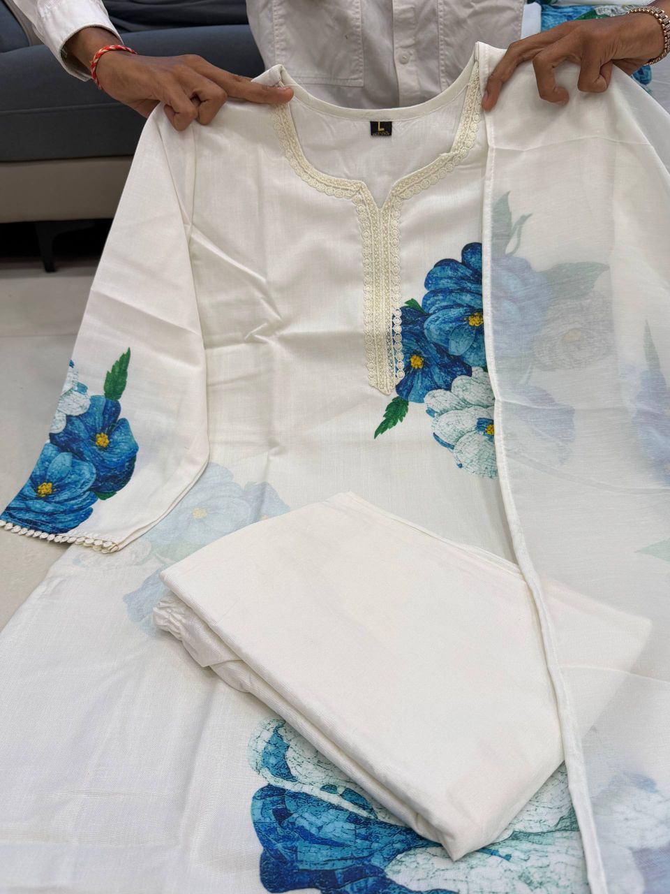 White embroidered outfit with blue floral patterns held by a person.