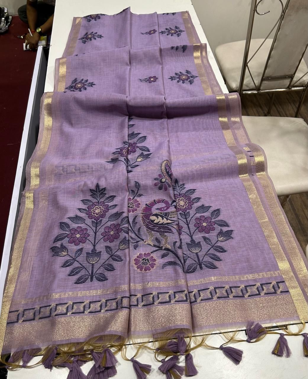 Purple saree with floral and peacock designs on a white table.