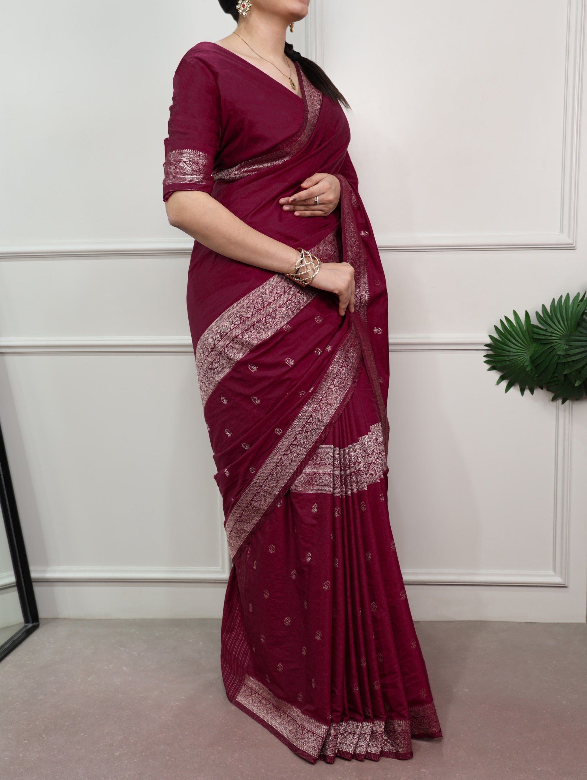 Woman wearing a maroon saree with white border against a white wall.
