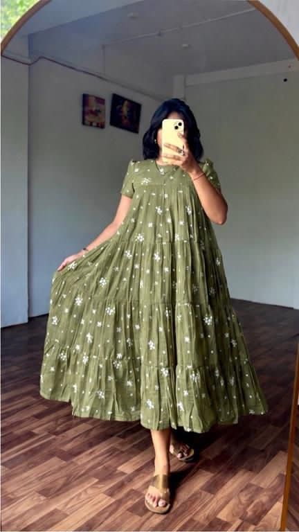 Person wearing a green dress with white patterns, standing in a room with wooden flooring.