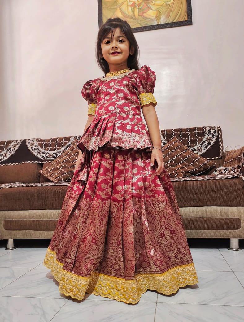 Young girl in a traditional red outfit standing in a room with a sofa and decorative wall art.