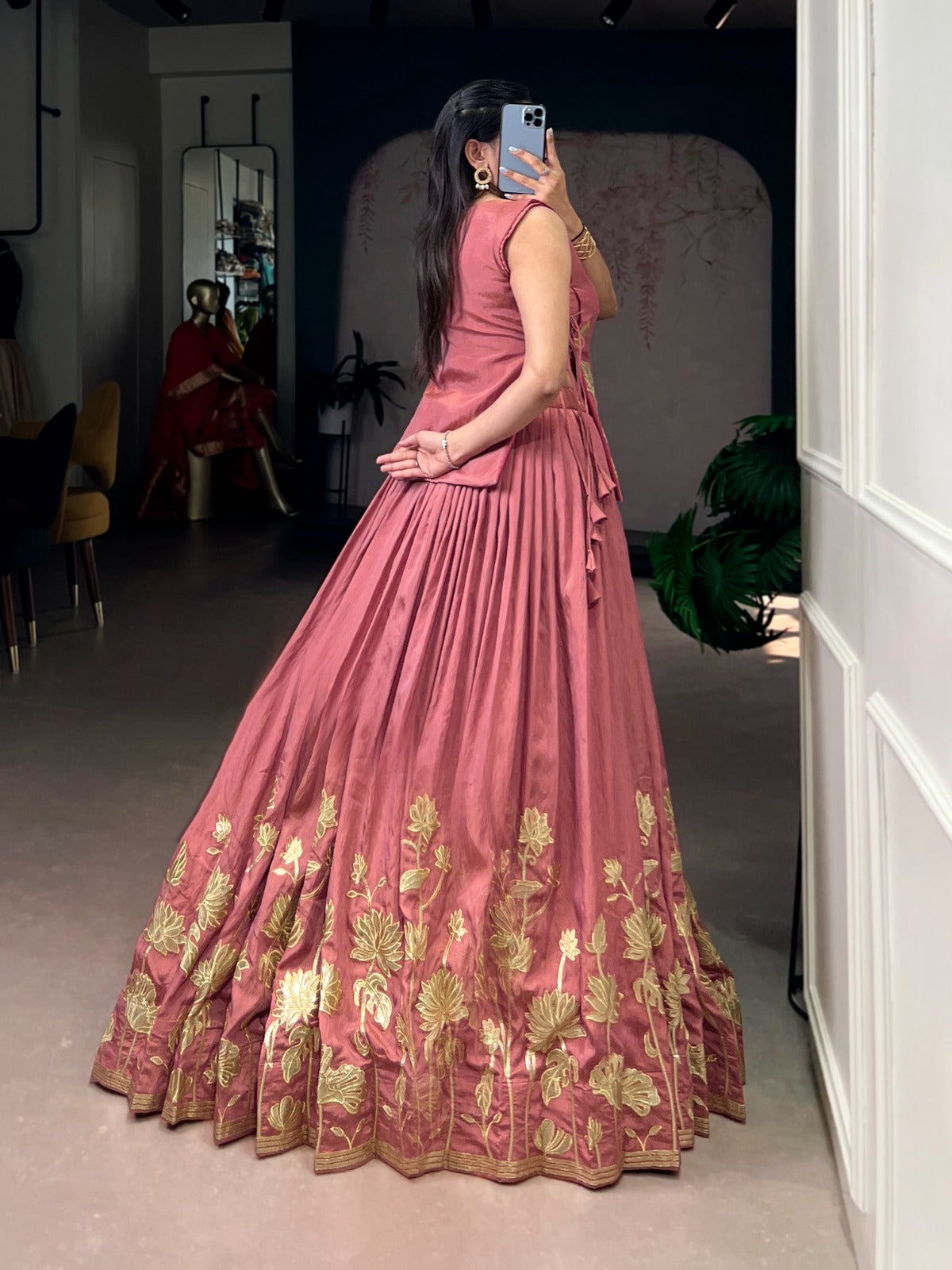 Woman in a peach gown with gold embroidery standing in a room.