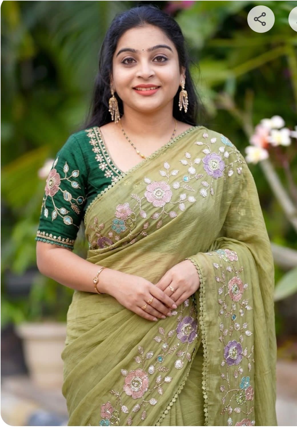 Woman wearing a olive green saree with floral patterns against a blurred natural background