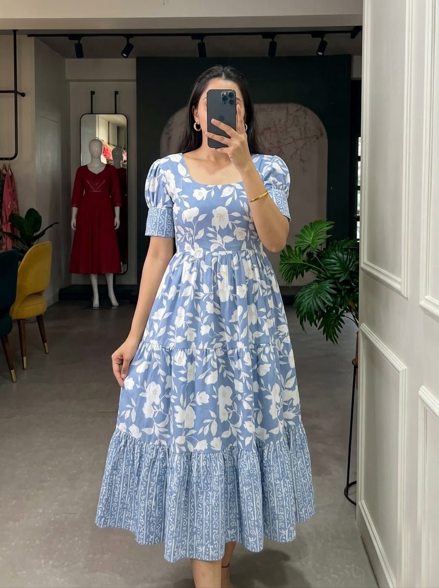 Woman wearing a Light blue floral dress taking a mirror selfie in a store.