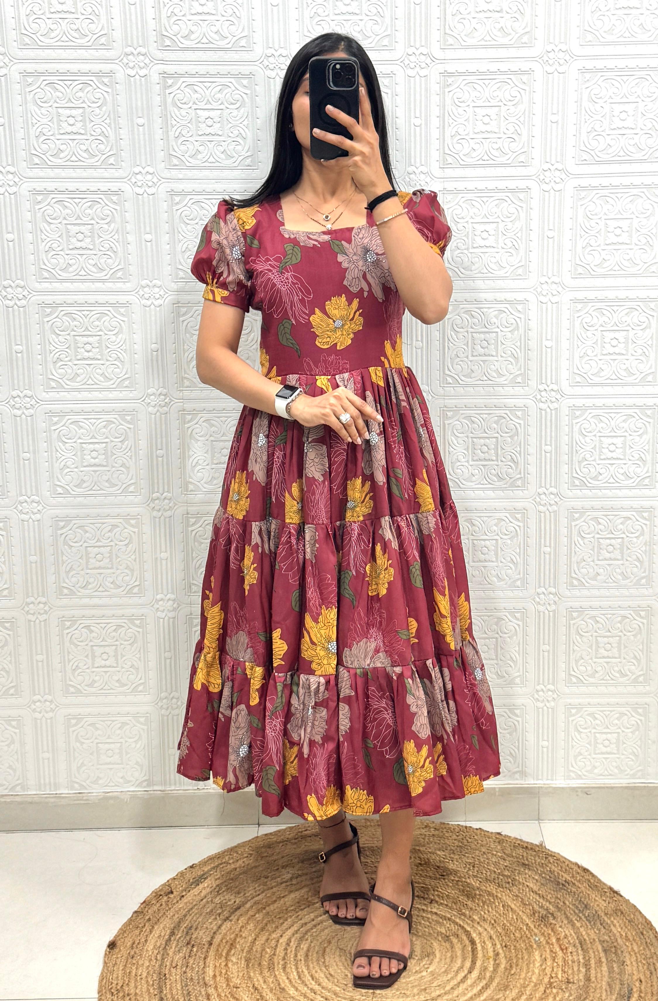 Woman wearing a maroon floral dress taking a mirror selfie against a white tiled wall.