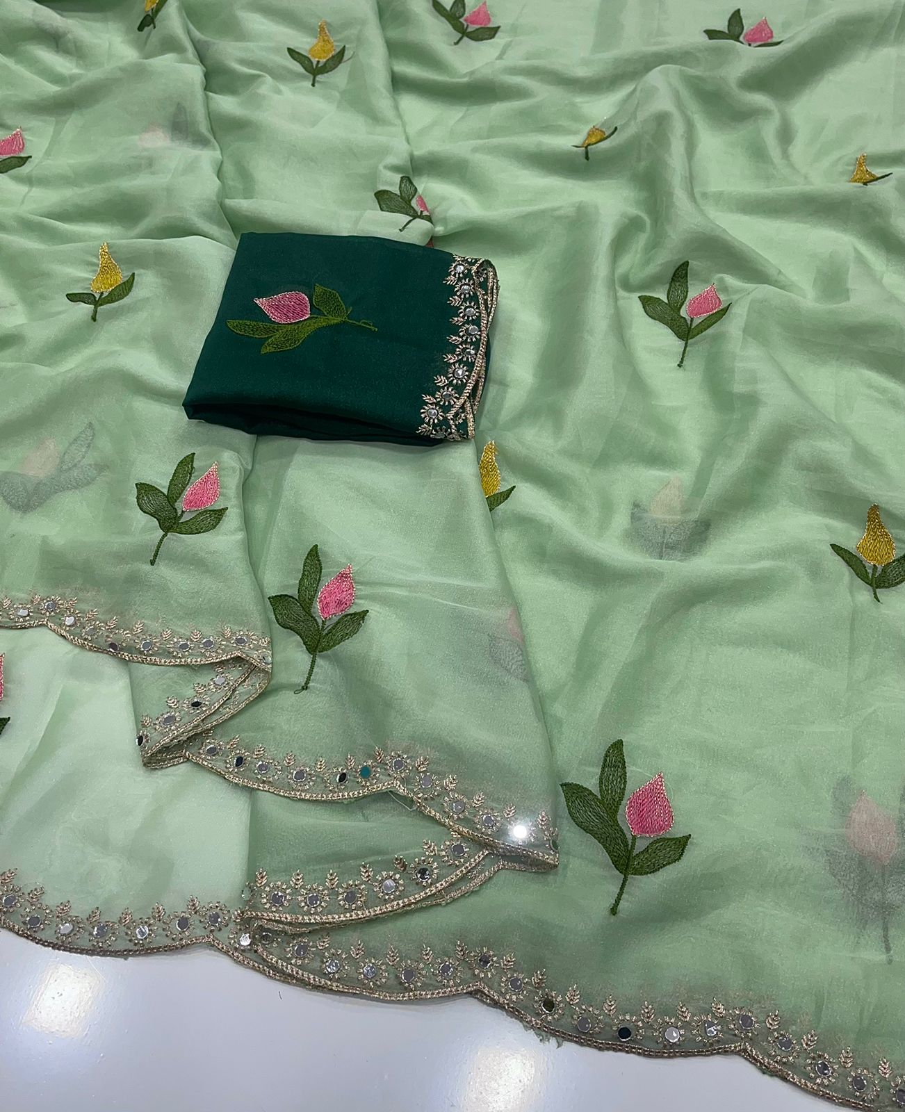 Decorative light green fabric with floral patterns and a green blouse on a matching fabric background.