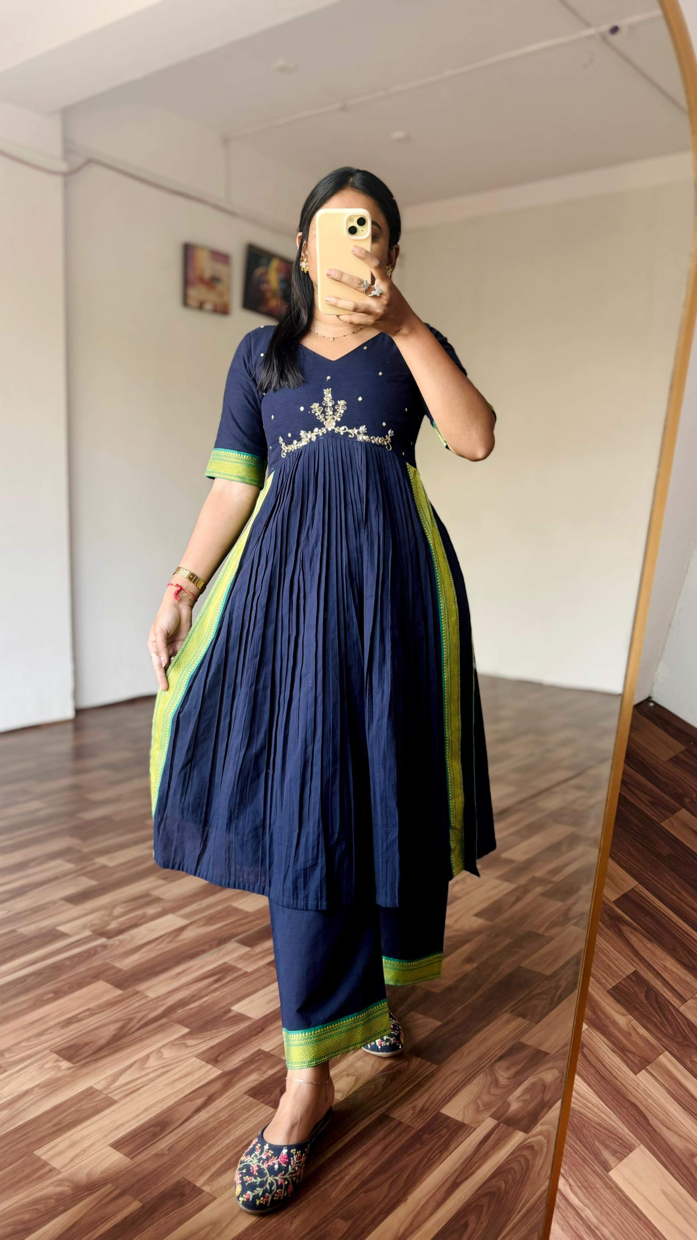 Person wearing a navy blue dress with green accents in a room.