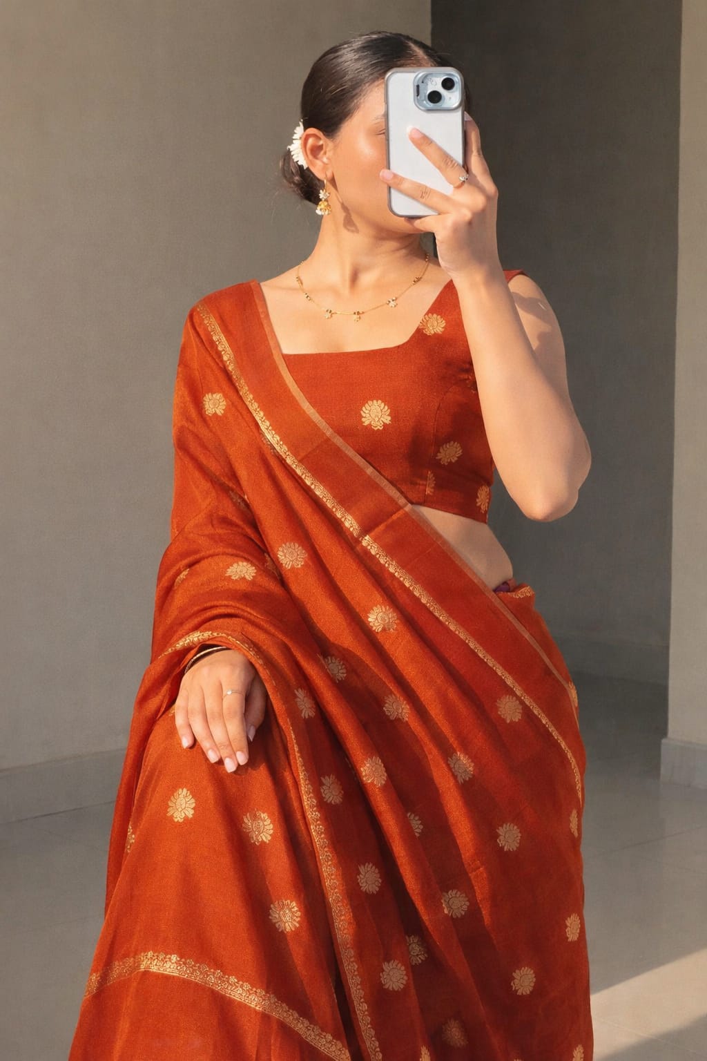 Woman wearing a Rust orange saree with gold patterns, taking a mirror selfie.