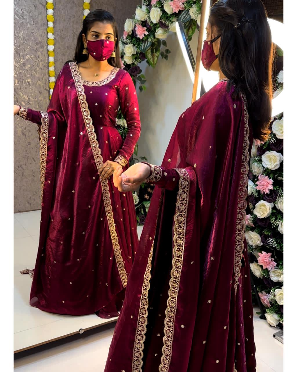 Woman in a wine traditional outfit with gold embroidery, standing in front of a mirror.