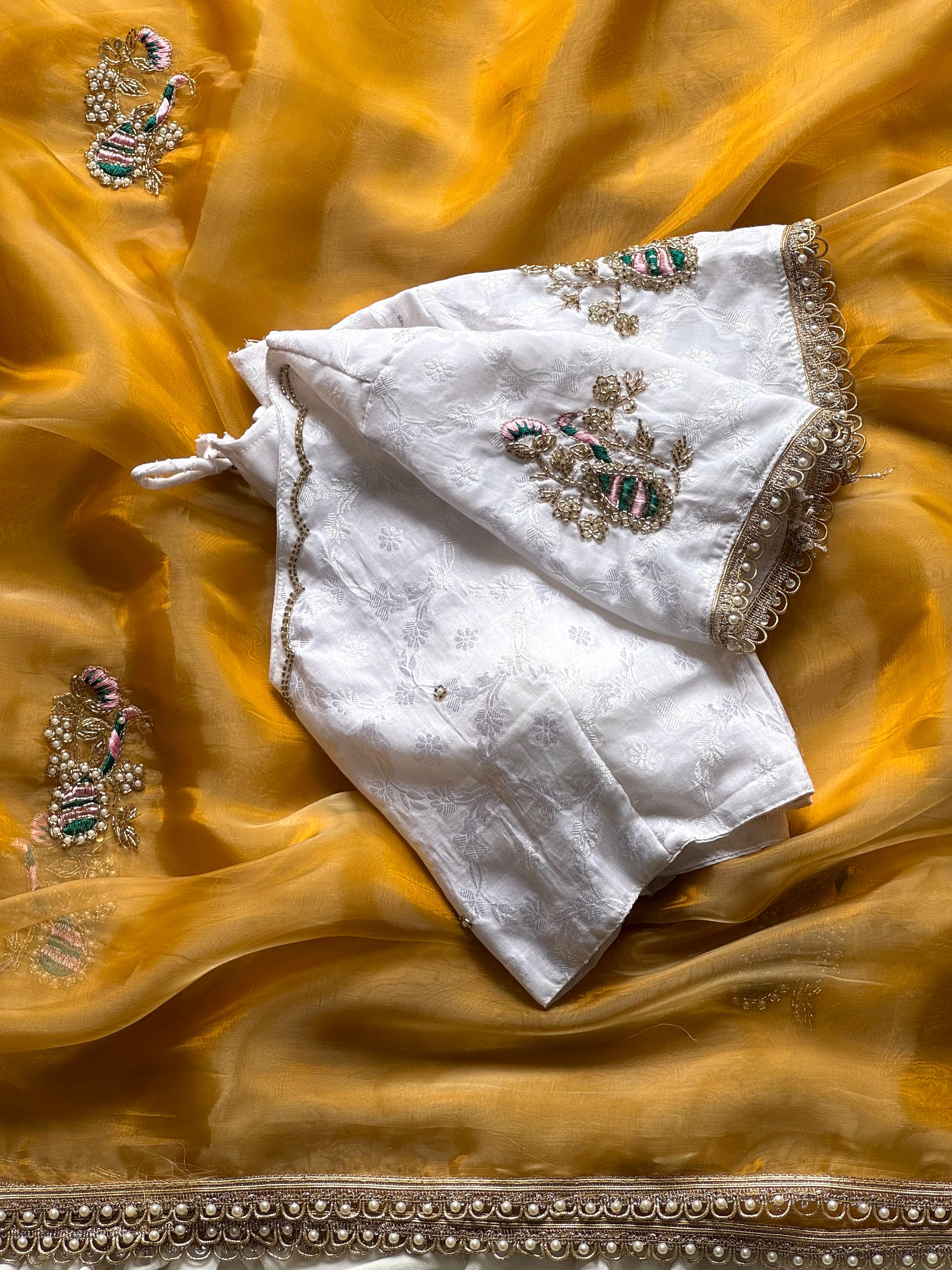 White embroidered blouse with gold details on a mustard yellow fabric background