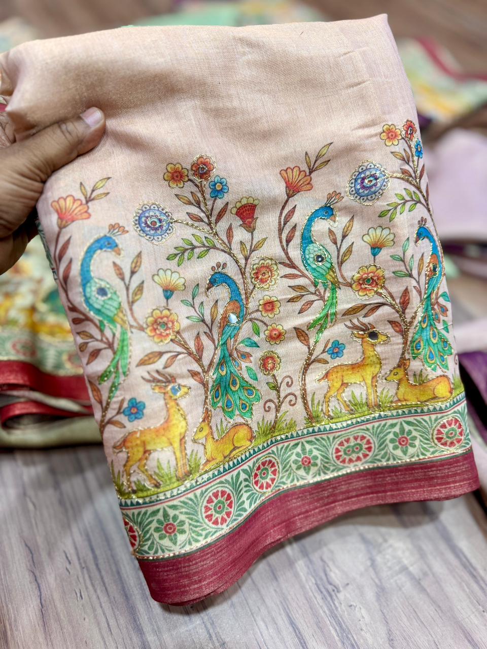 Beige fabric with peacock and deer design held by a hand on a wooden surface.