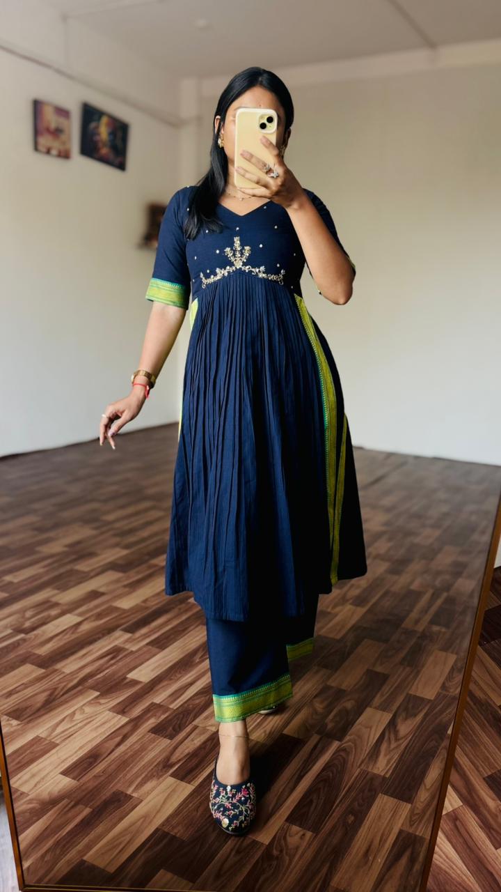 Person wearing a navy blue dress with green accents in a room with wooden flooring.