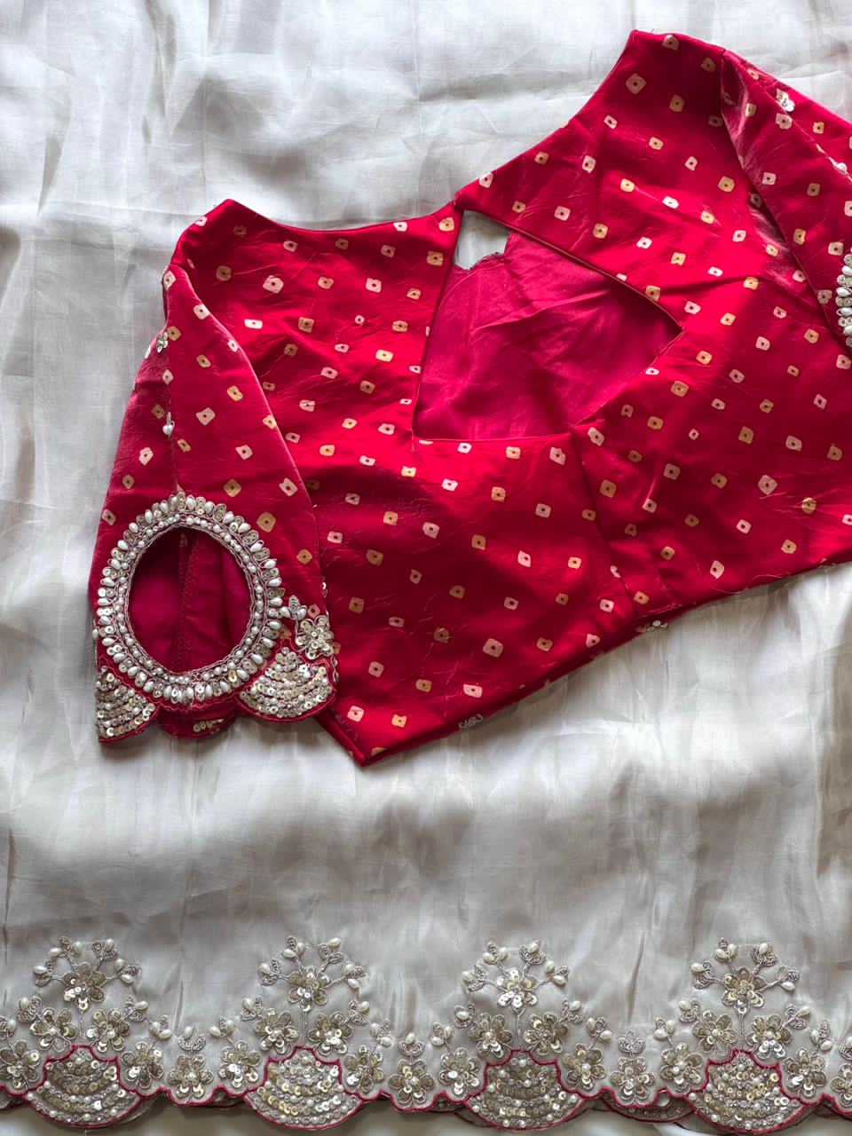 Red blouse with gold patterns and a silver necklace on a white fabric background