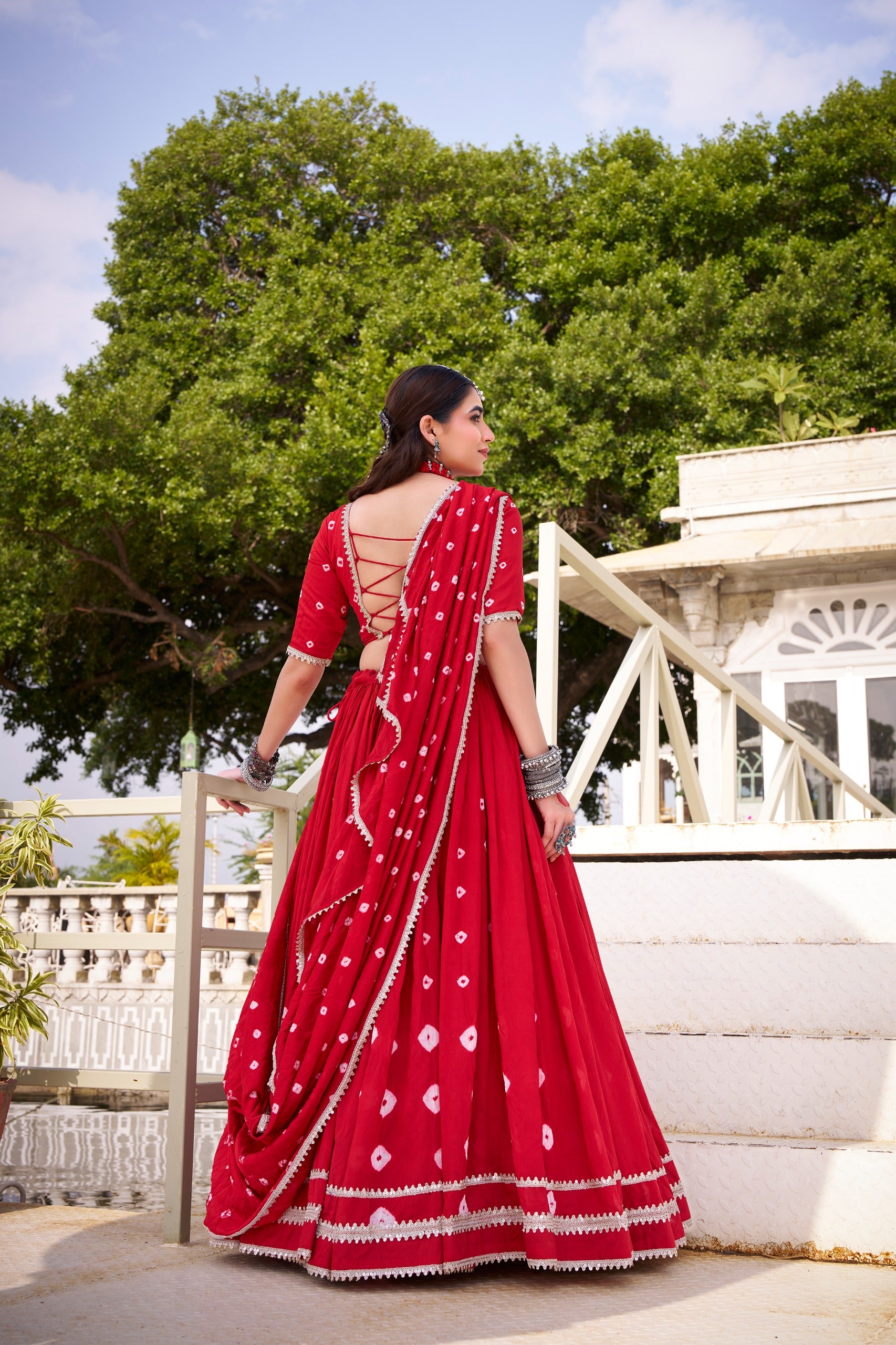 Woman in a red lehenga with white patterns standing outdoors with greenery in the background