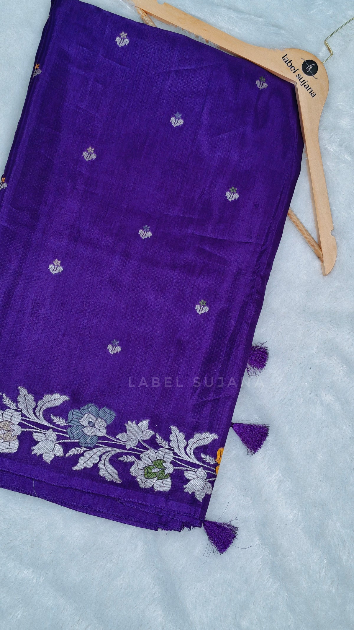 A folded purple silk saree with silver and white floral border 