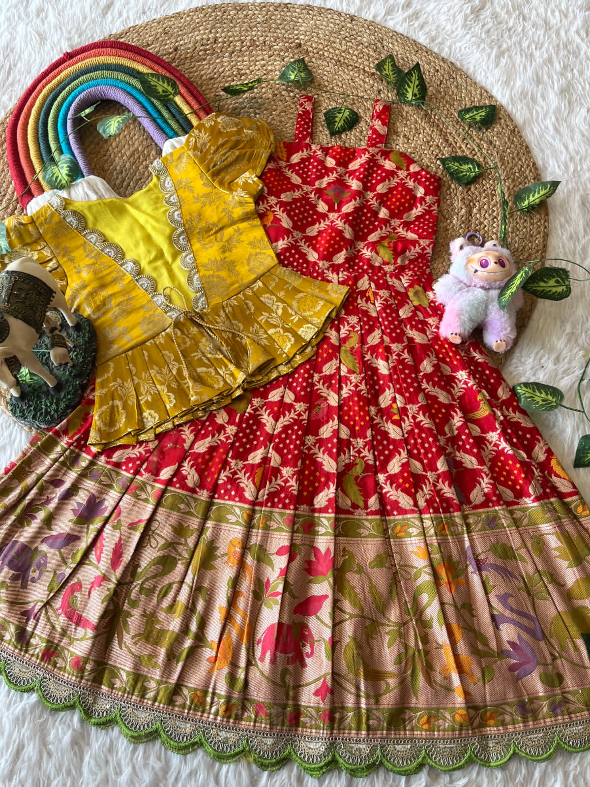 Colorful Red children's dress with a rainbow, teddy bear, and toys on a textured surface