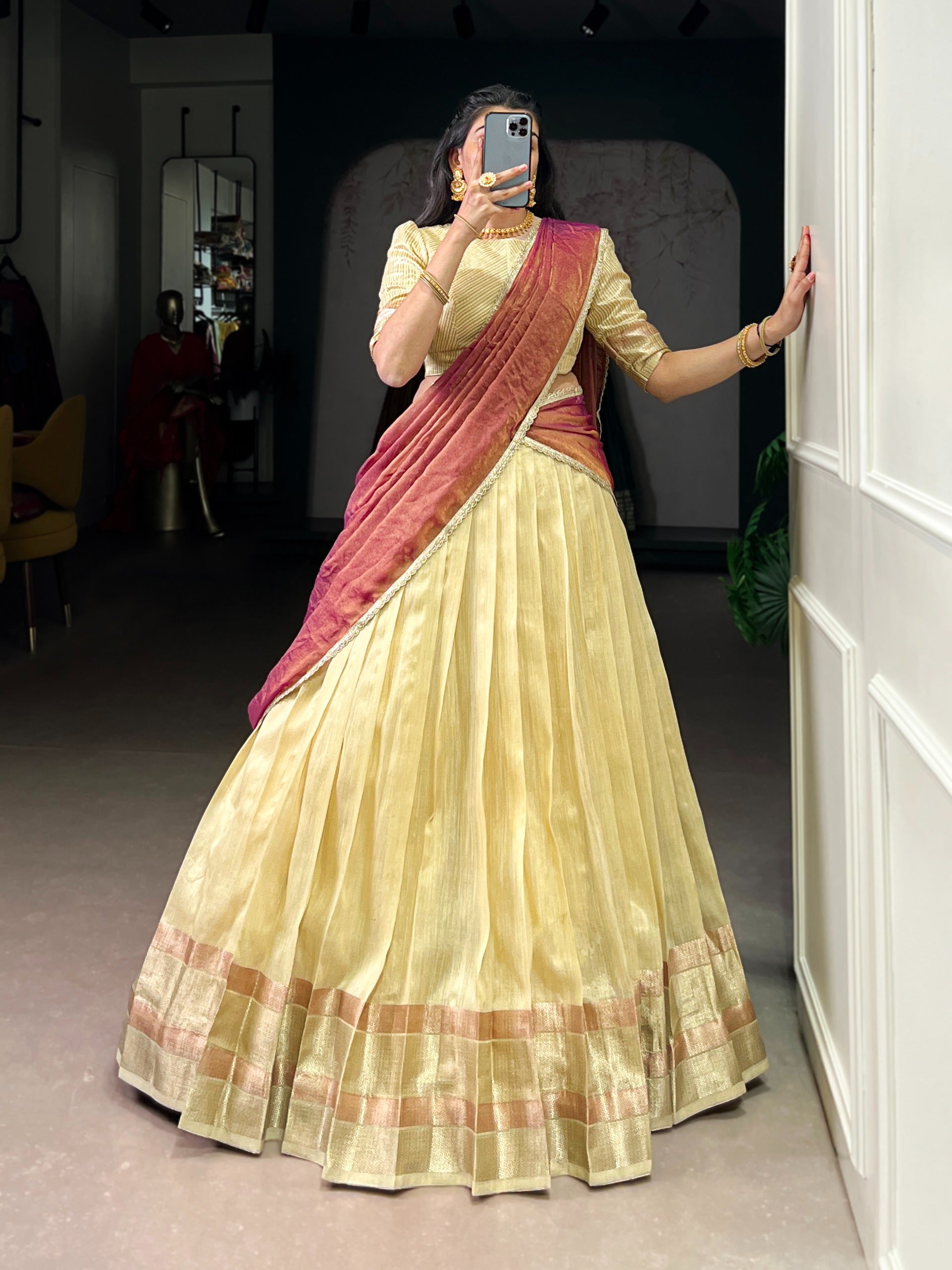 Woman wearing a traditional outfit with a red and beige saree in a room.